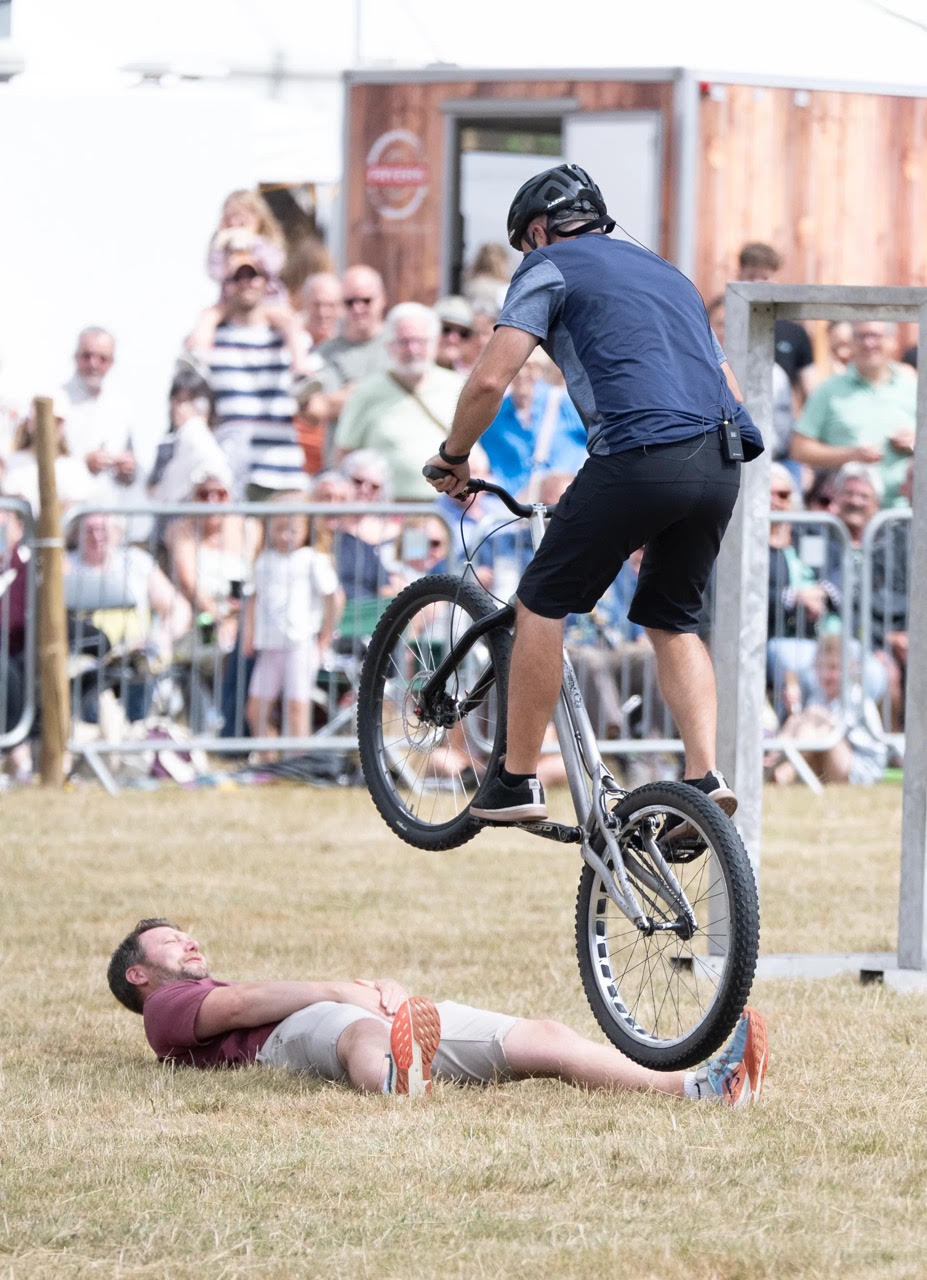 Cyclist in helmet performing trick over person lying on grass
