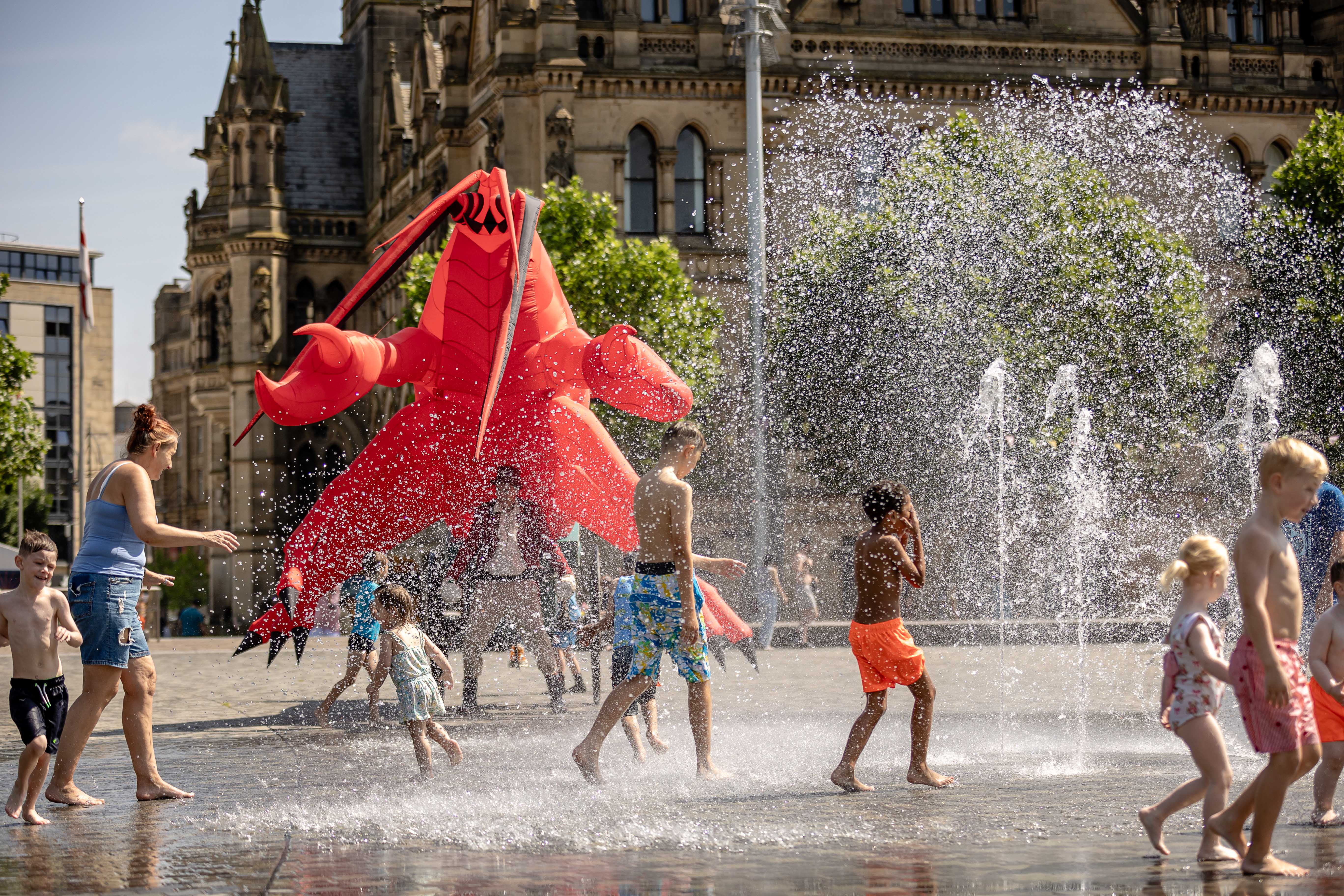 Children playing in fountains beside historic building with red sculpture