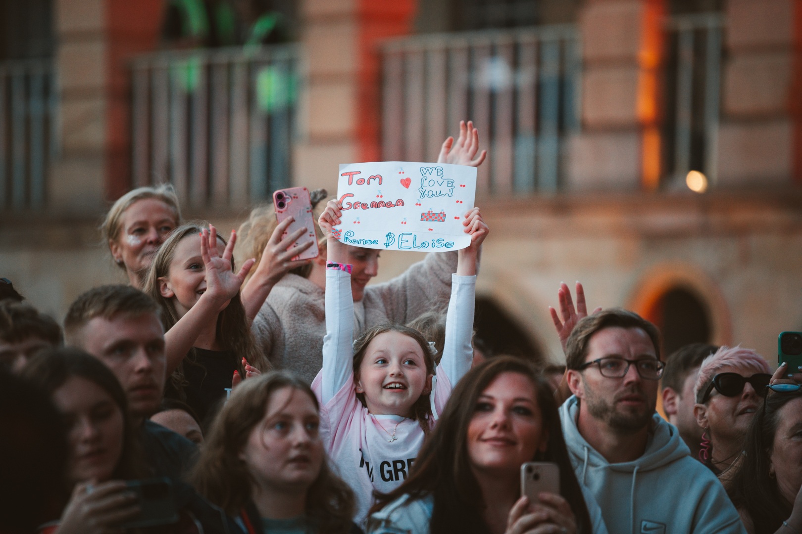 Excited crowd at outdoor event with girl holding sign
