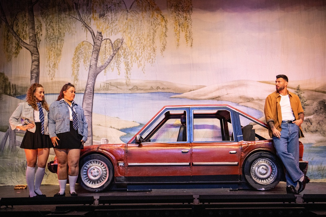 Theatre actors posing around a painted car on stage