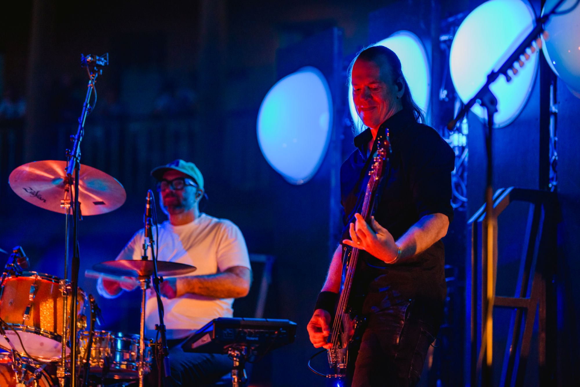 Two musicians on stage with drums and guitar under blue lights