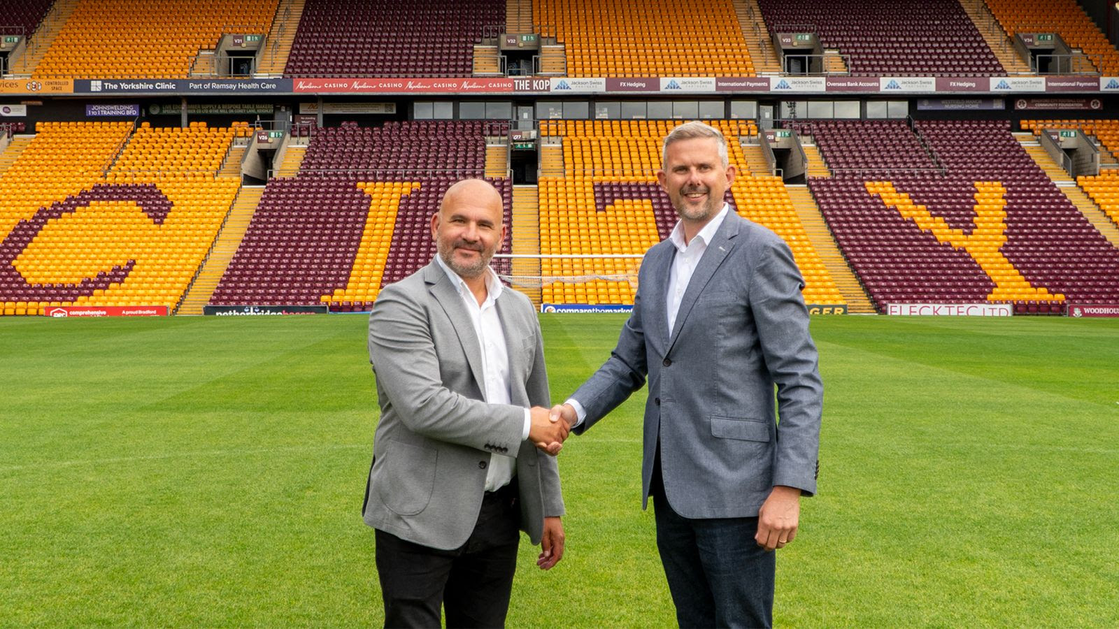 Two men in suits shaking hands on a football pitch