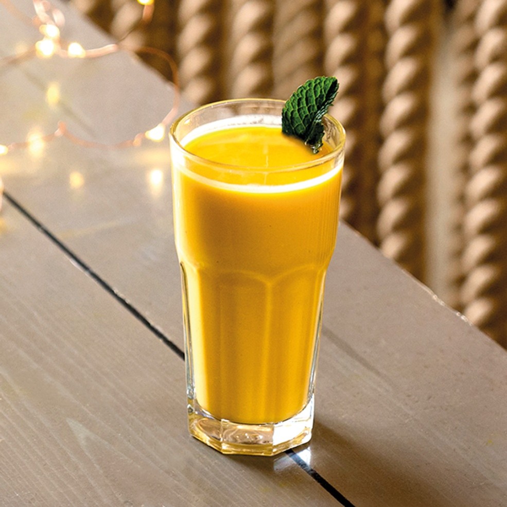 Tall glass of mango lassi with mint on wooden table