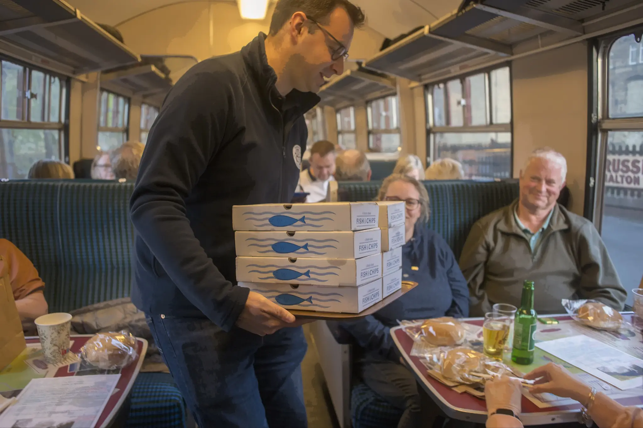 Server in vintage train carriage delivering fish and chips