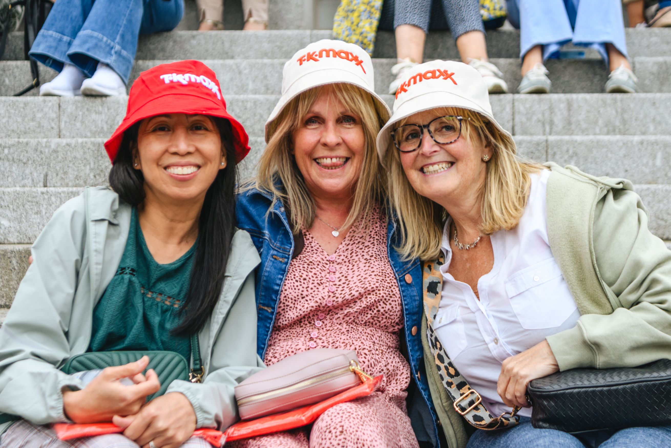 Three smiling women in bucket hats sitting on stone steps
