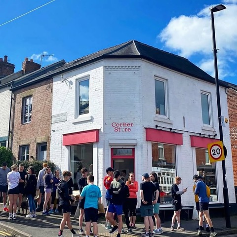 Group of people outside a white corner shop with red trim