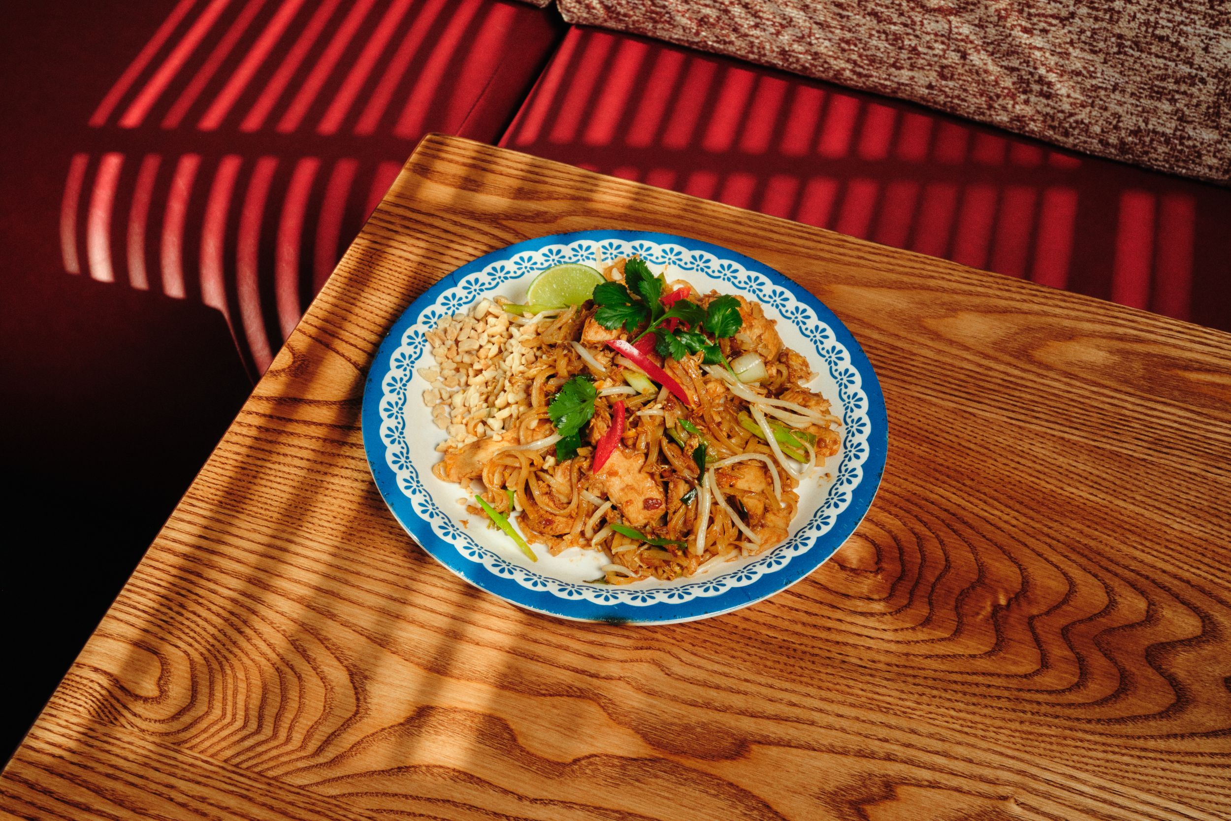 Plate of Pad Thai with lime and coriander on wooden table