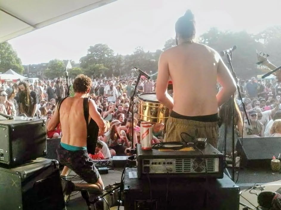 Outdoor music festival with shirtless musicians and large crowd
