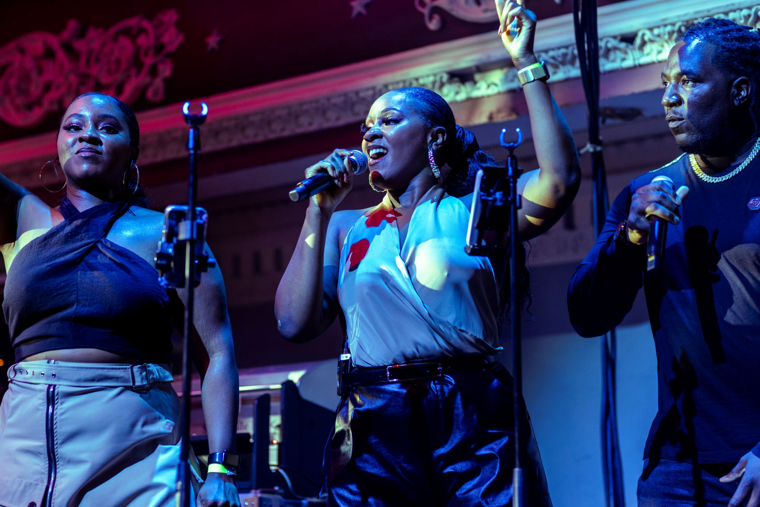 Three performers singing on stage with vibrant lighting