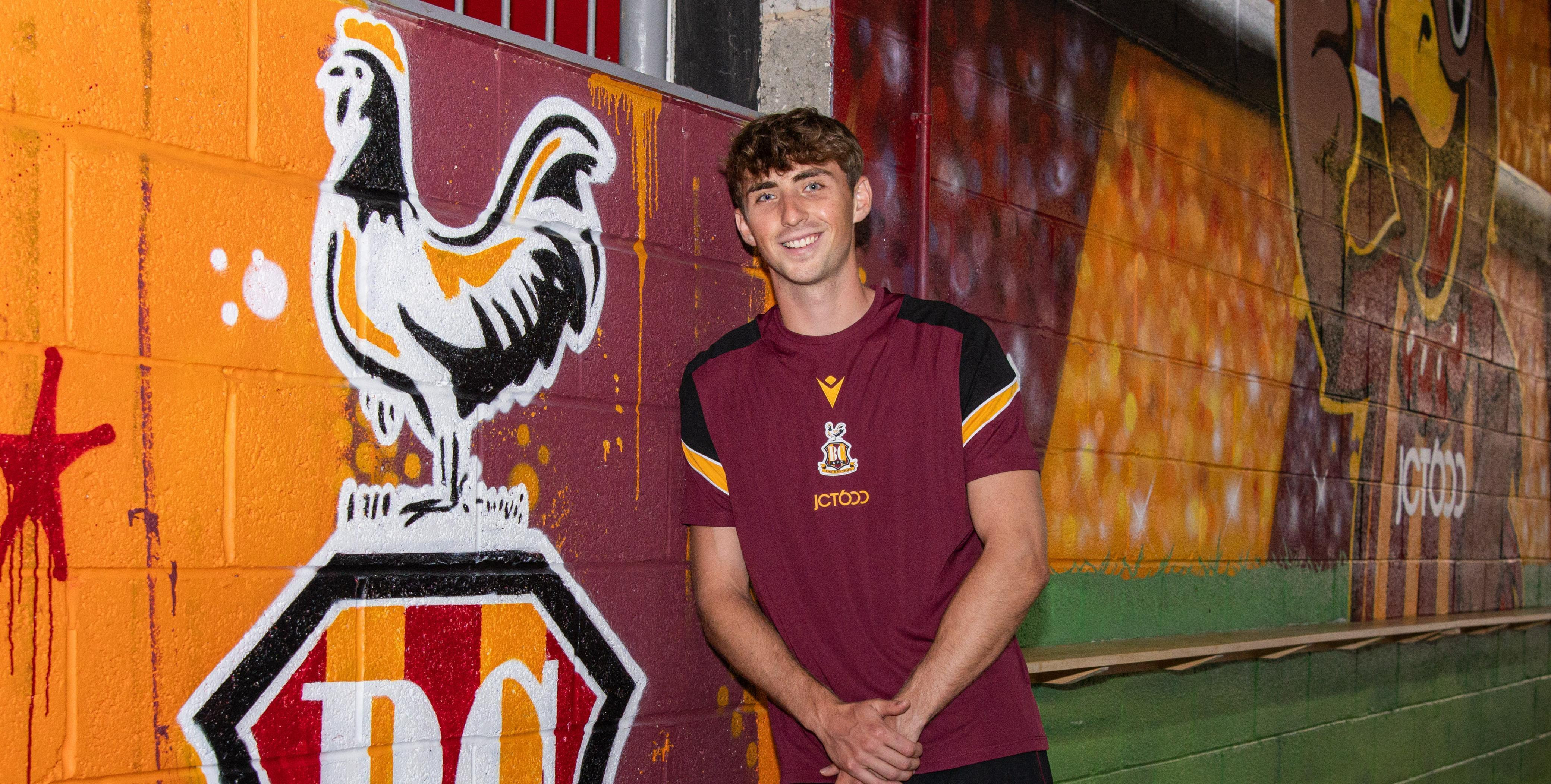 Young man in maroon sports shirt next to vibrant rooster mural