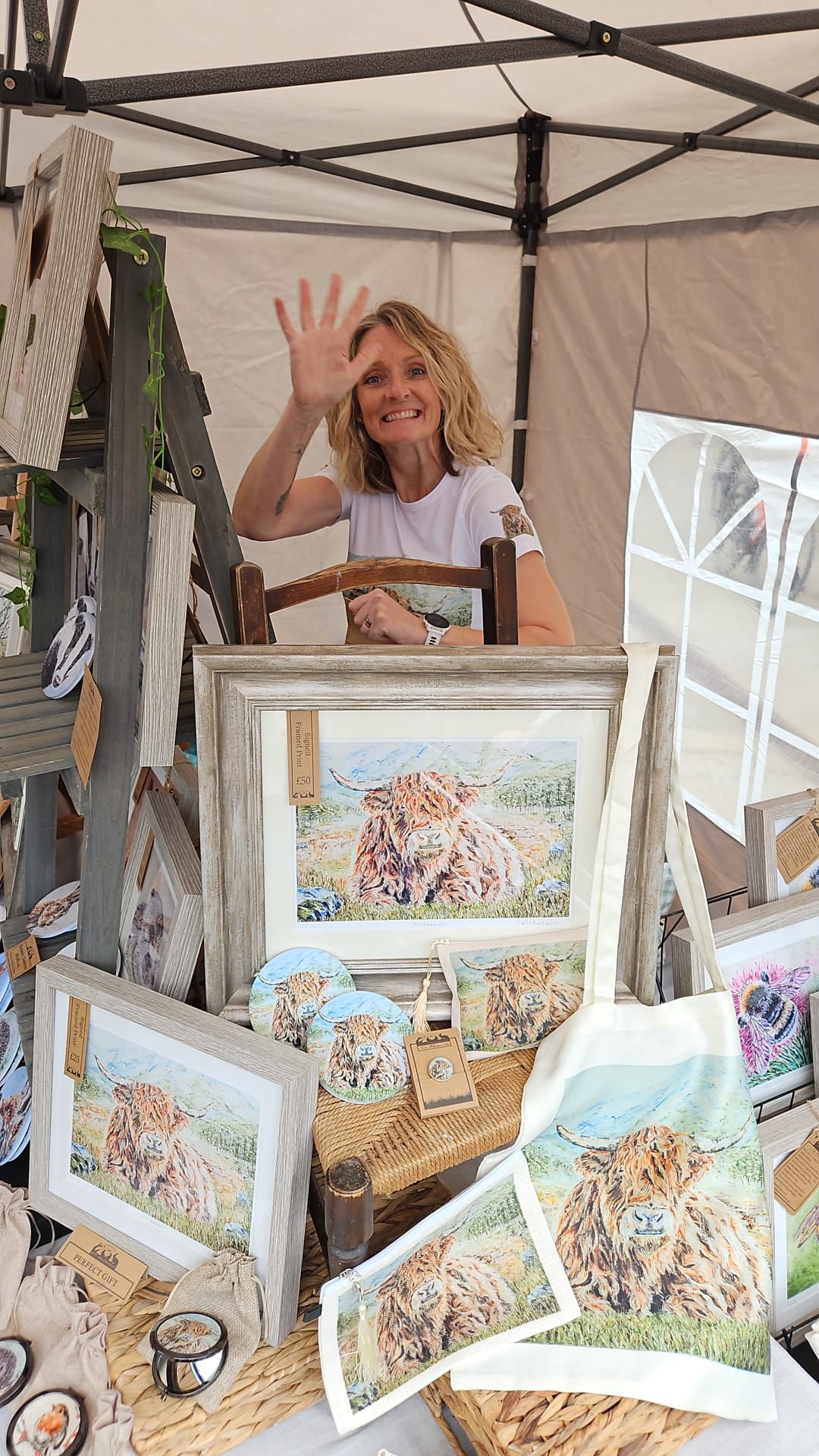 Smiling vendor waving at craft stall with lion artwork and prints