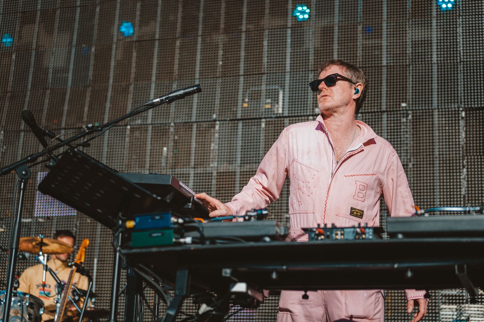 Musician in pink jumpsuit playing keyboard on outdoor stage
