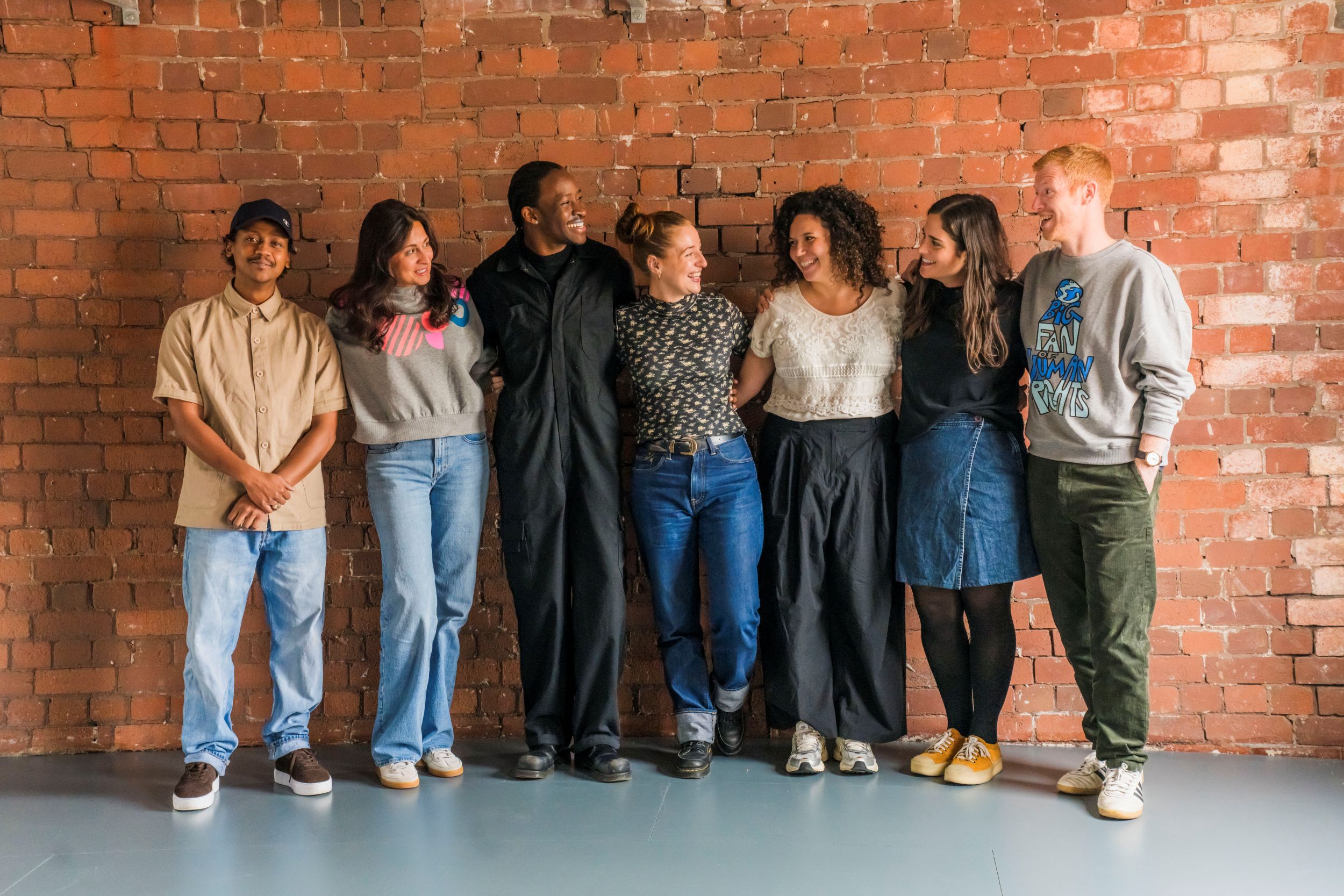 Group of seven people smiling against a red brick wall