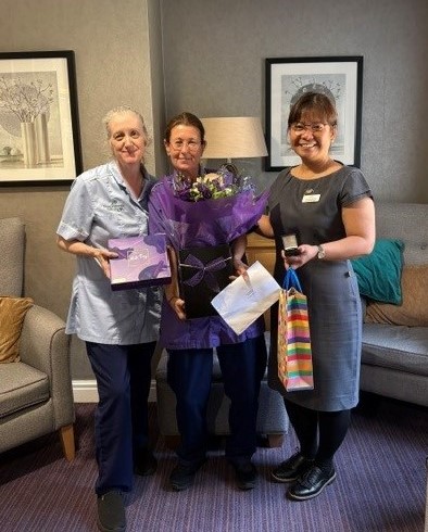 Three smiling women standing in a cozy room holding gifts