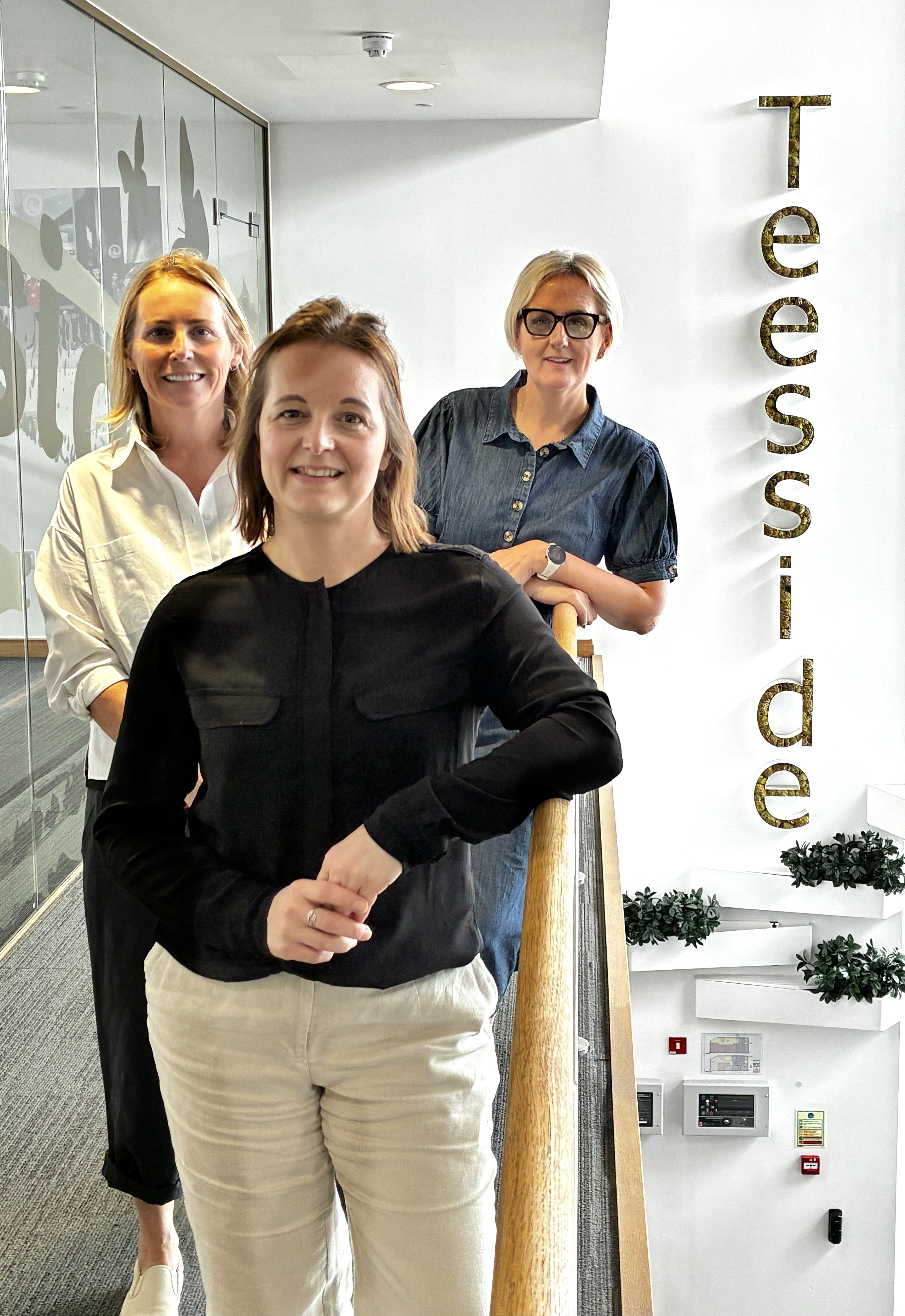 Three women standing in a modern hallway with Teesside sign