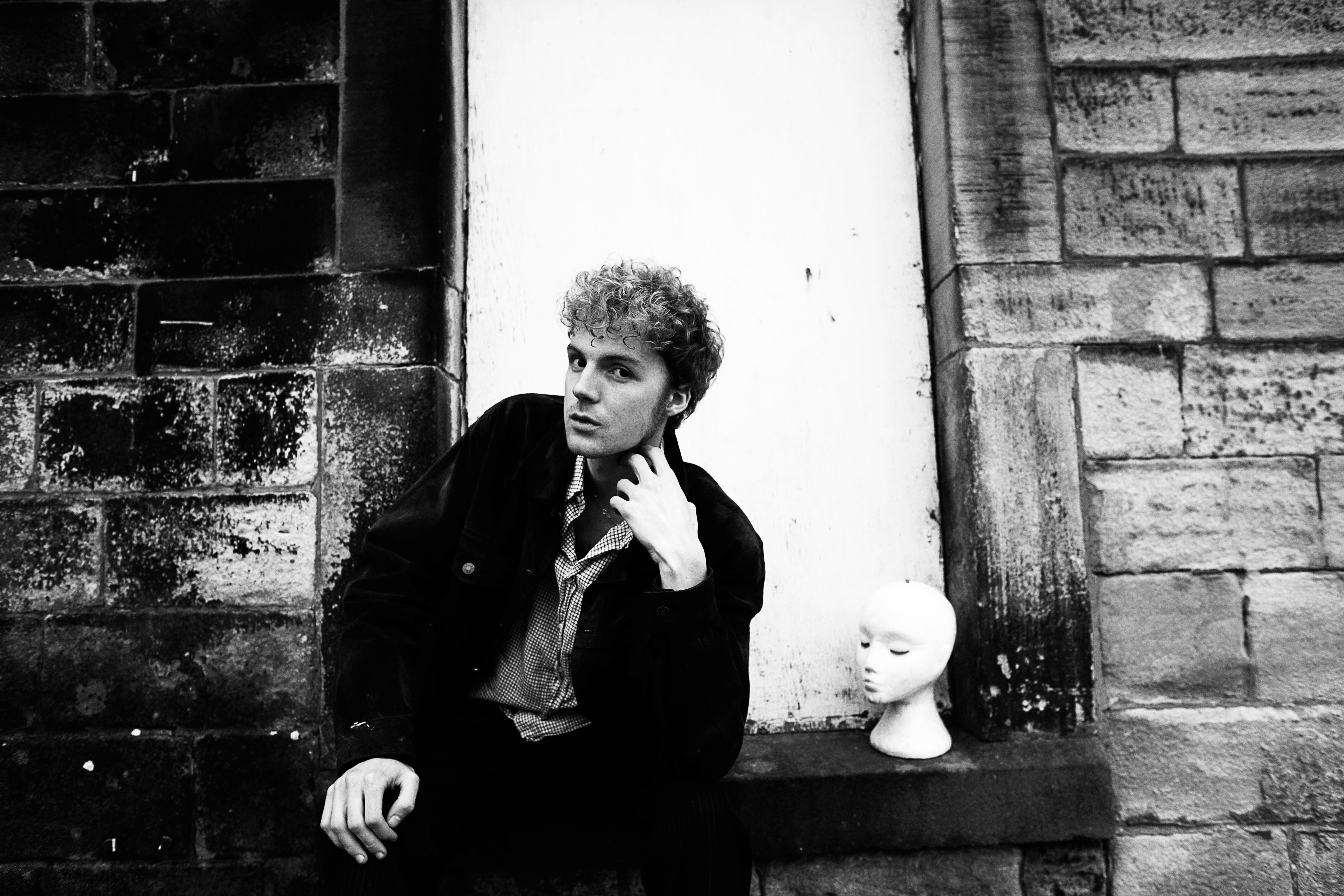 Young man in thoughtful pose against stone wall with mannequin head