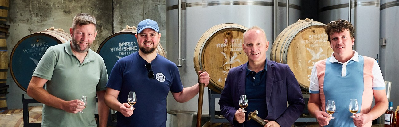 Four men tasting whisky in a Yorkshire distillery with barrels