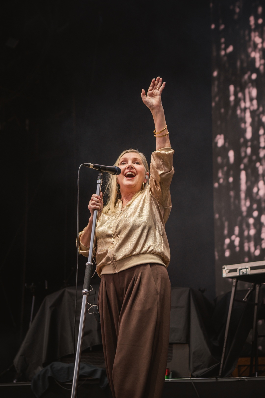 Woman in gold blouse singing on stage with microphone
