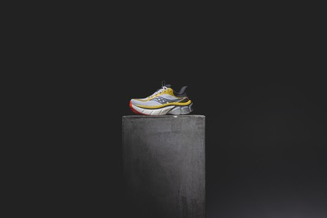 Yellow running shoe displayed on concrete pedestal against black background