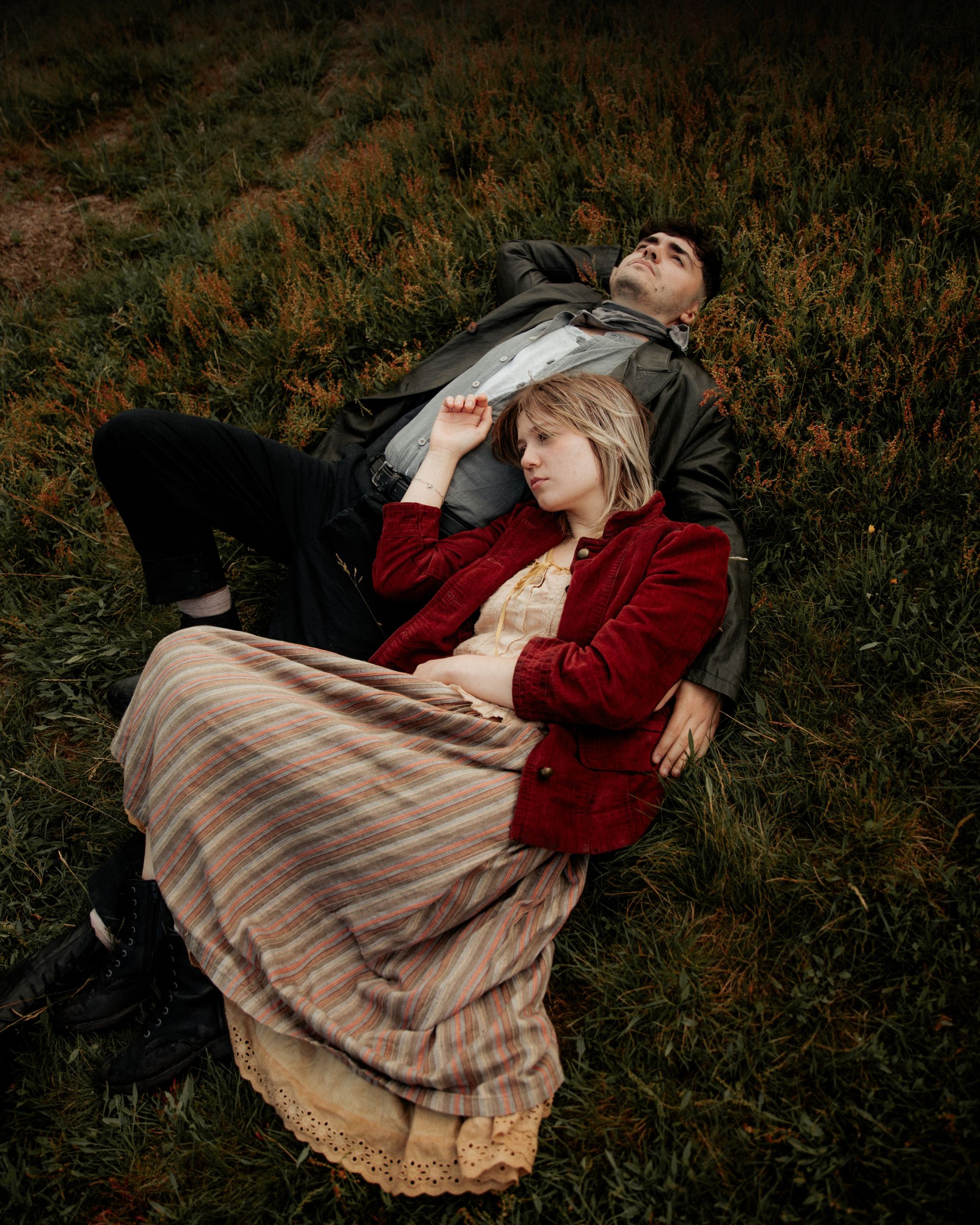 Couple lying on grassy hillside in casual vintage attire