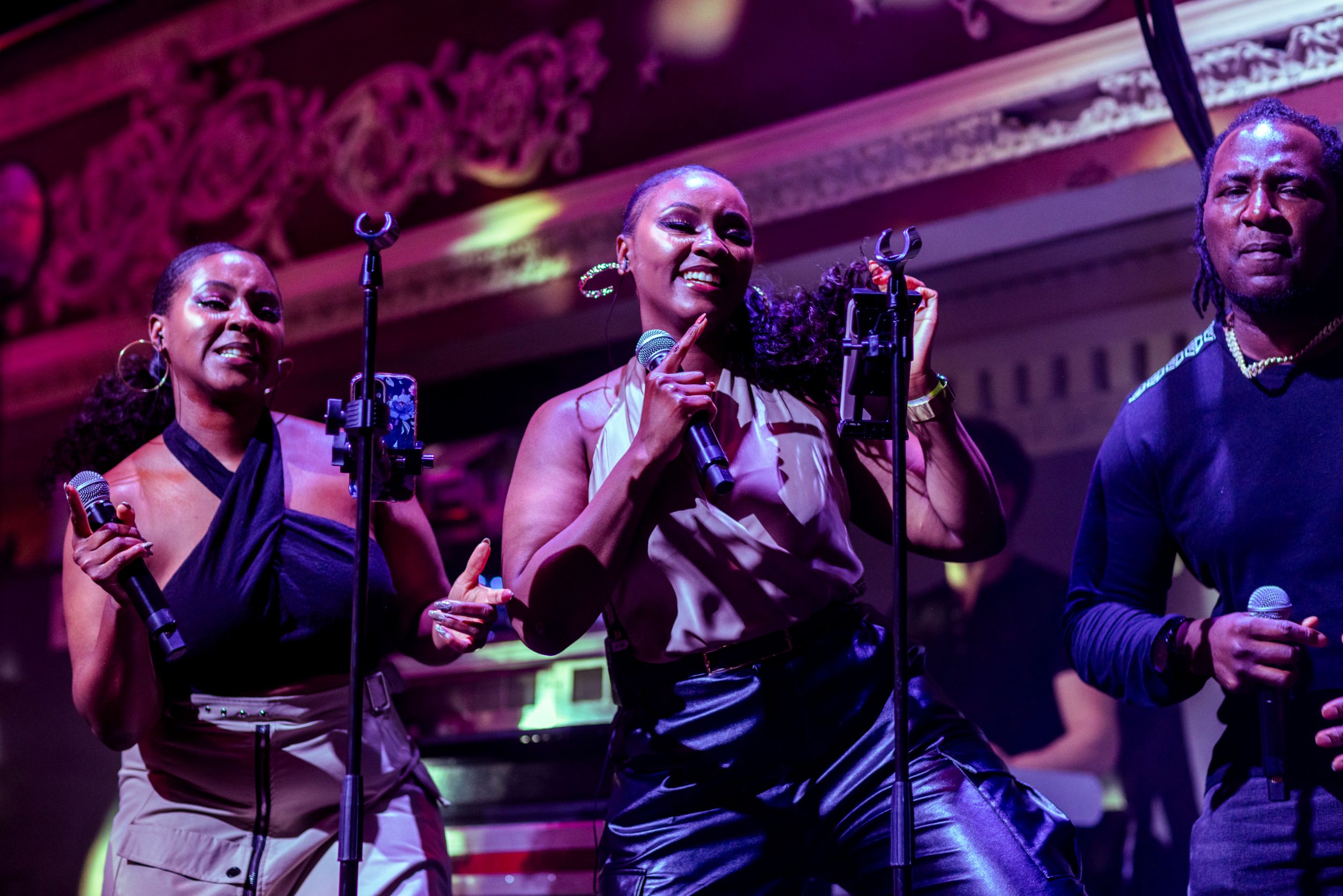 Three singers performing energetically on a vibrant stage