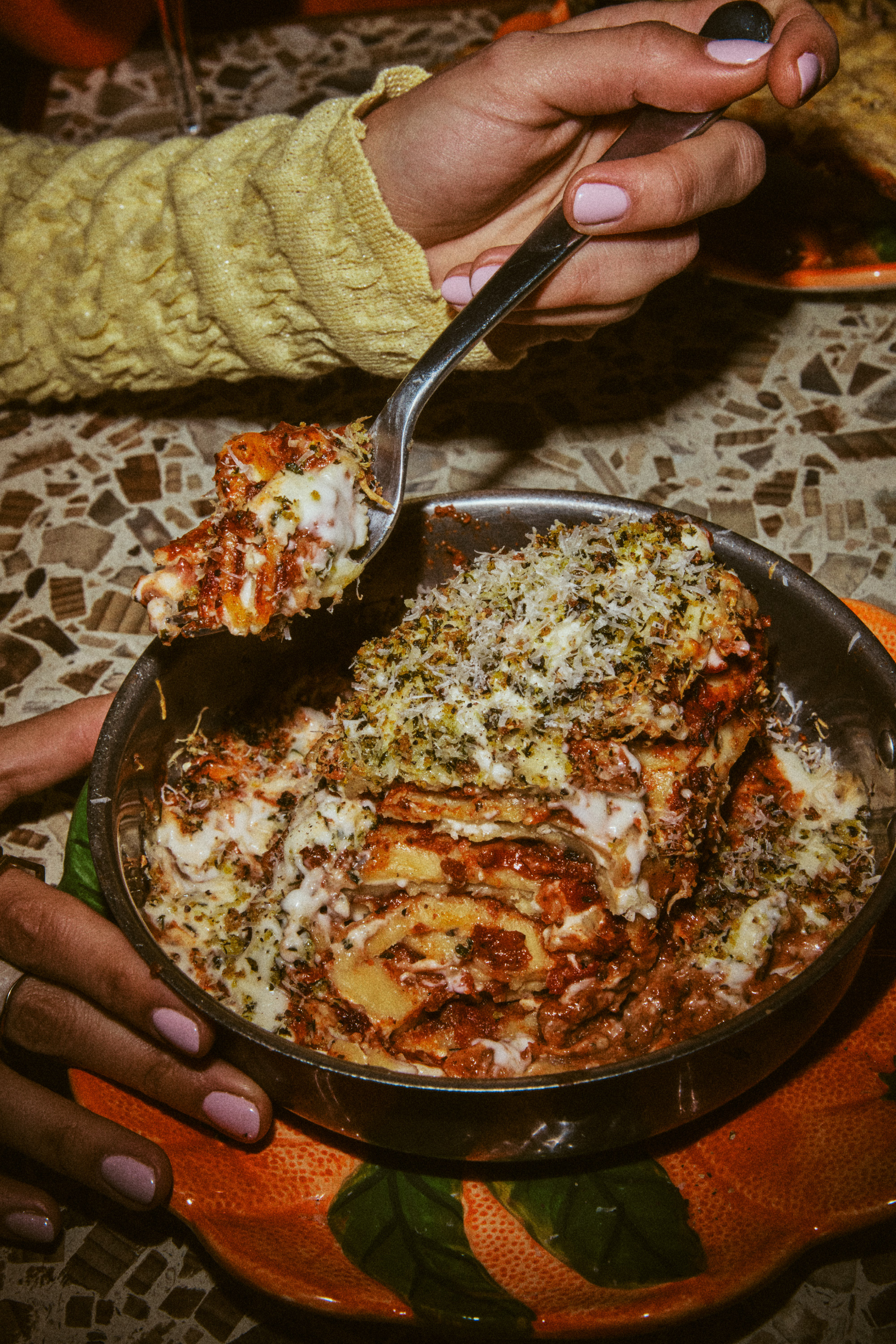 Close-up of hands serving lasagna with grated cheese