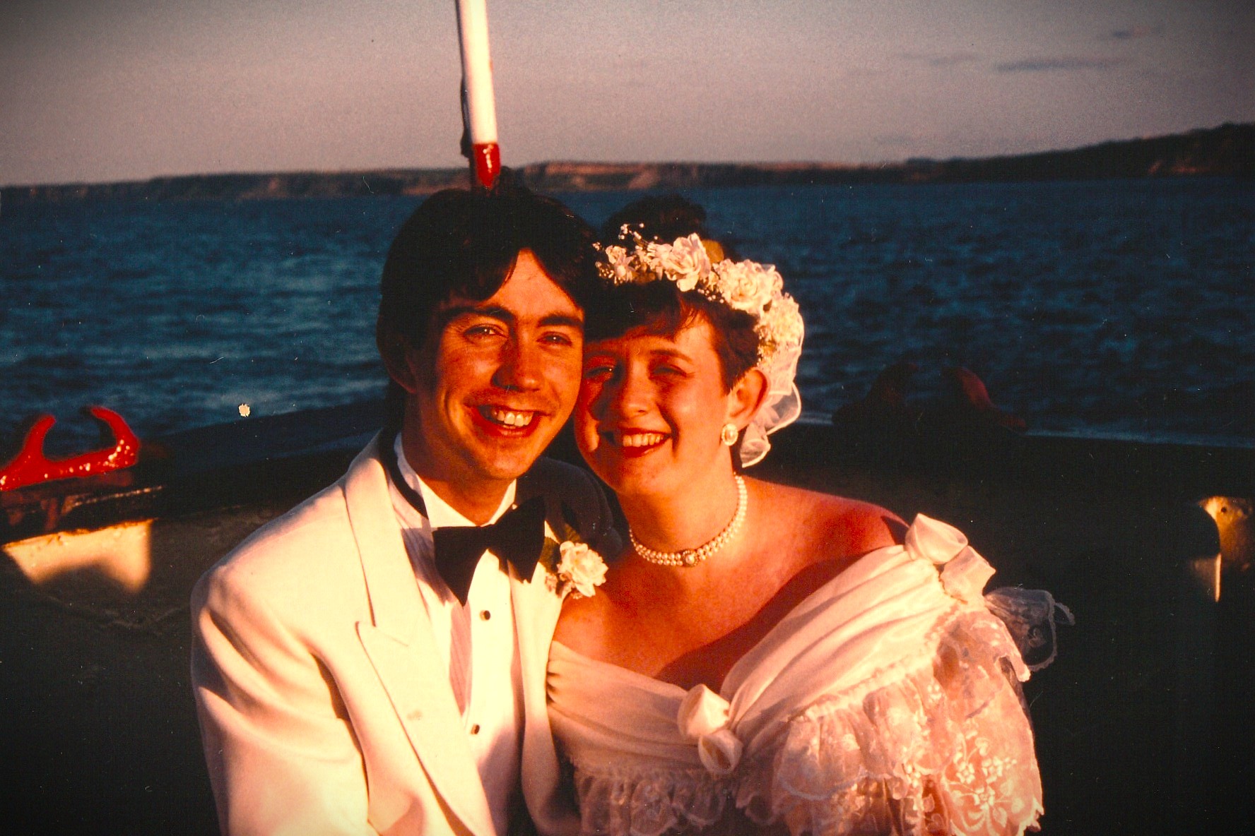 Smiling couple in wedding attire on boat at sea during sunset
