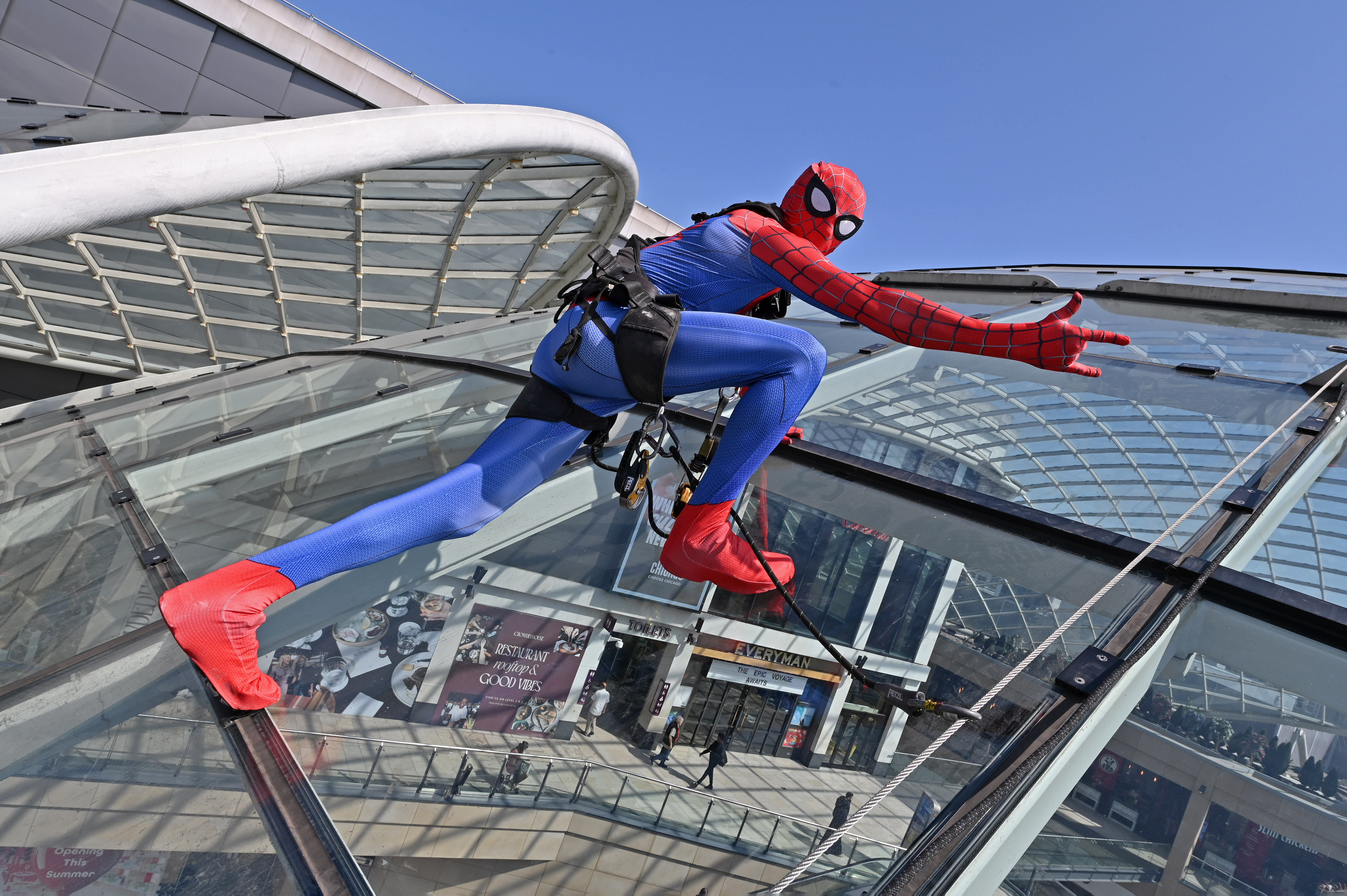 Person in superhero costume scaling glass canopy at shopping centre