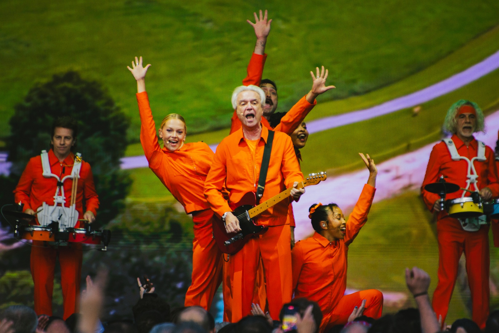Musicians in bright orange outfits performing energetically on stage