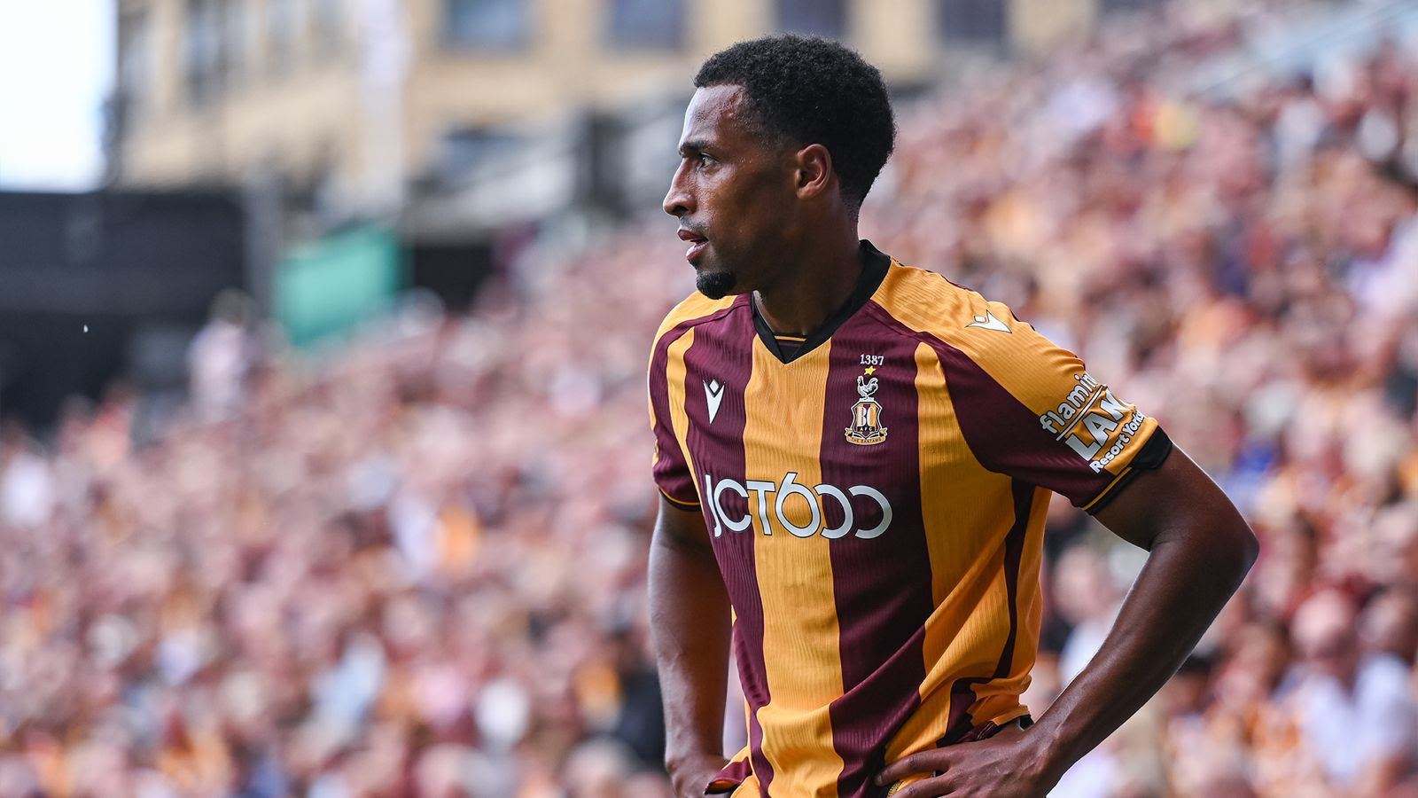 Footballer in claret and amber kit during a match at crowded stadium