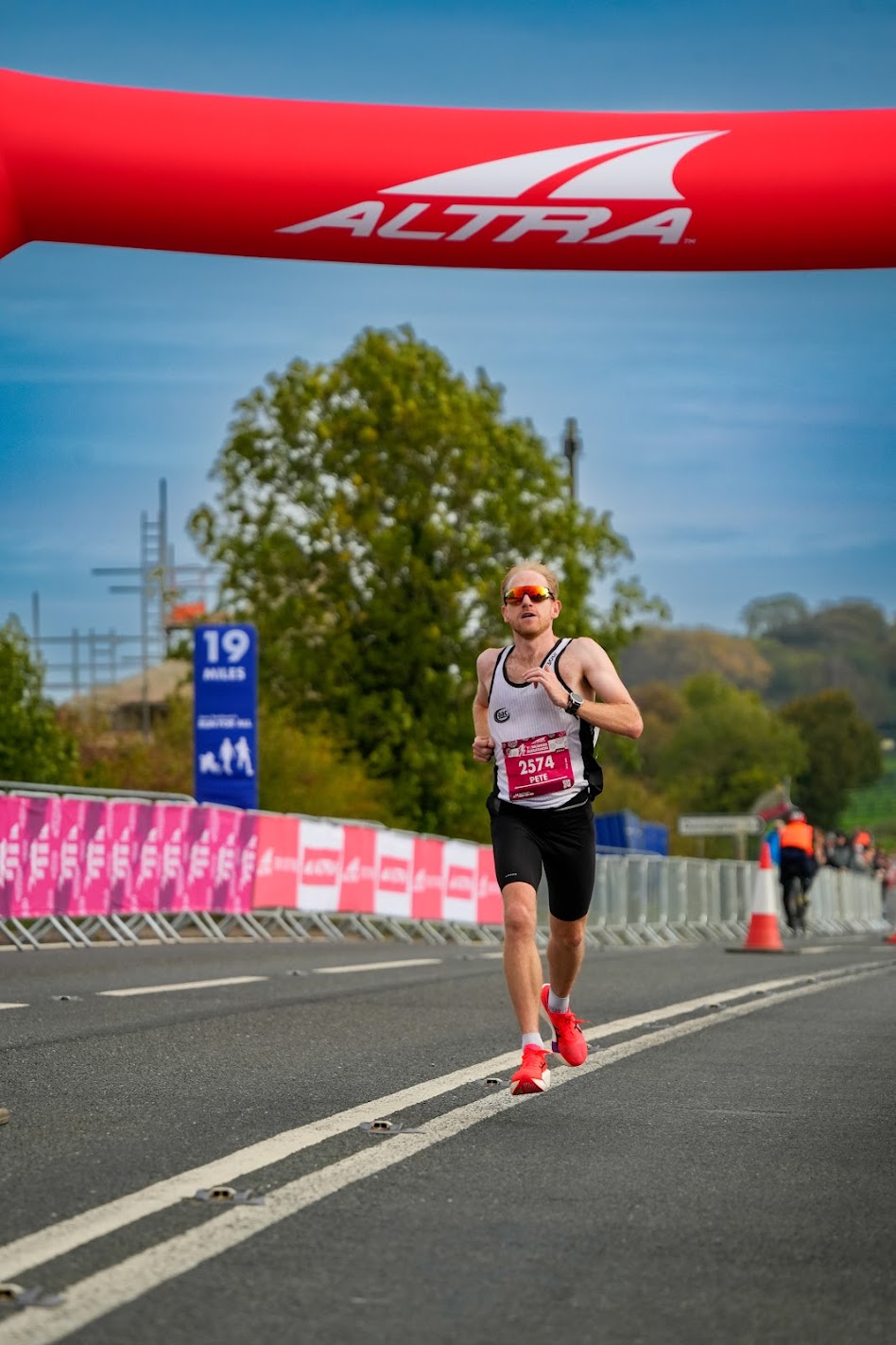 Runner in race passes under red arch on rural road with trees