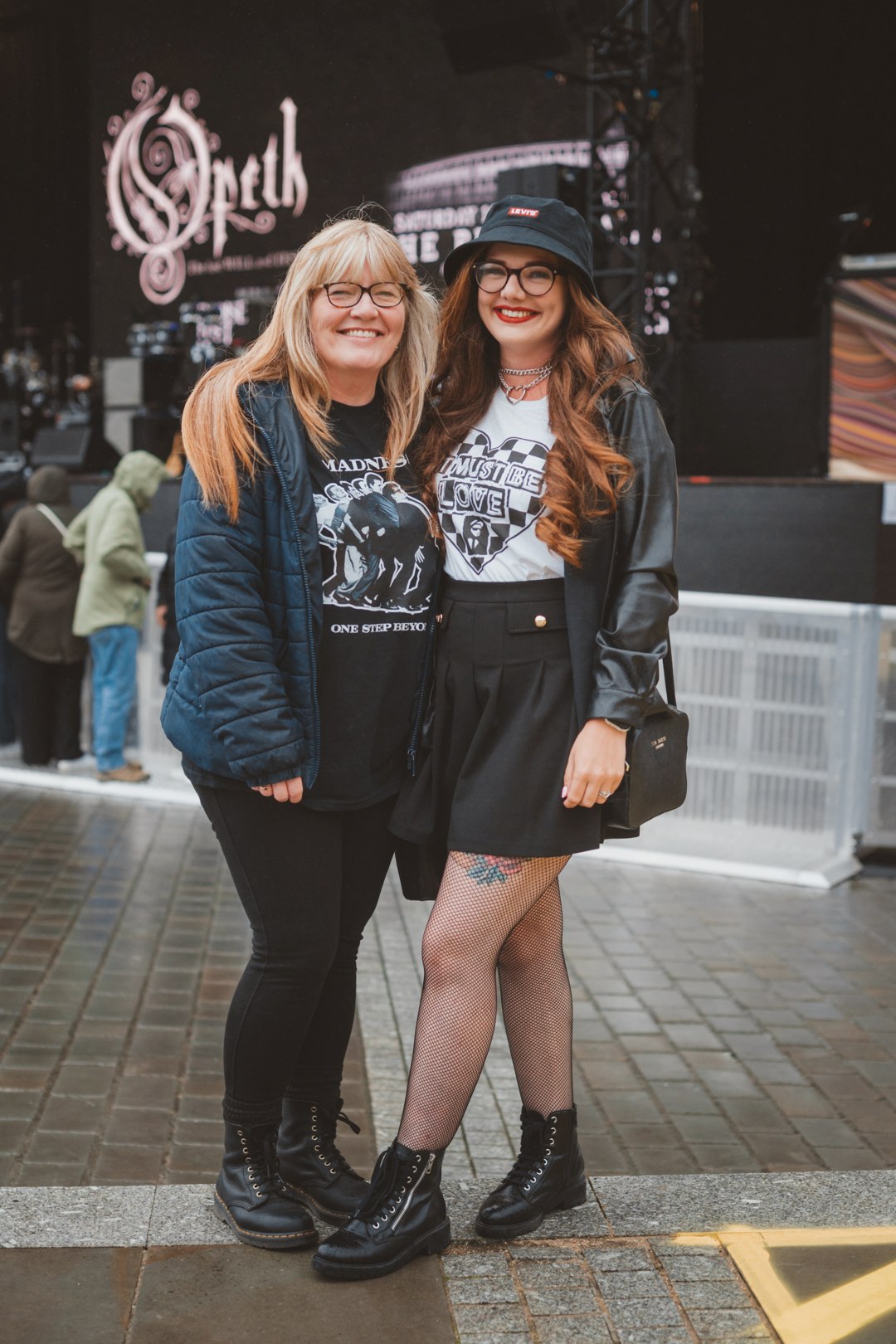 Two women in band t-shirts smiling at an outdoor music festival