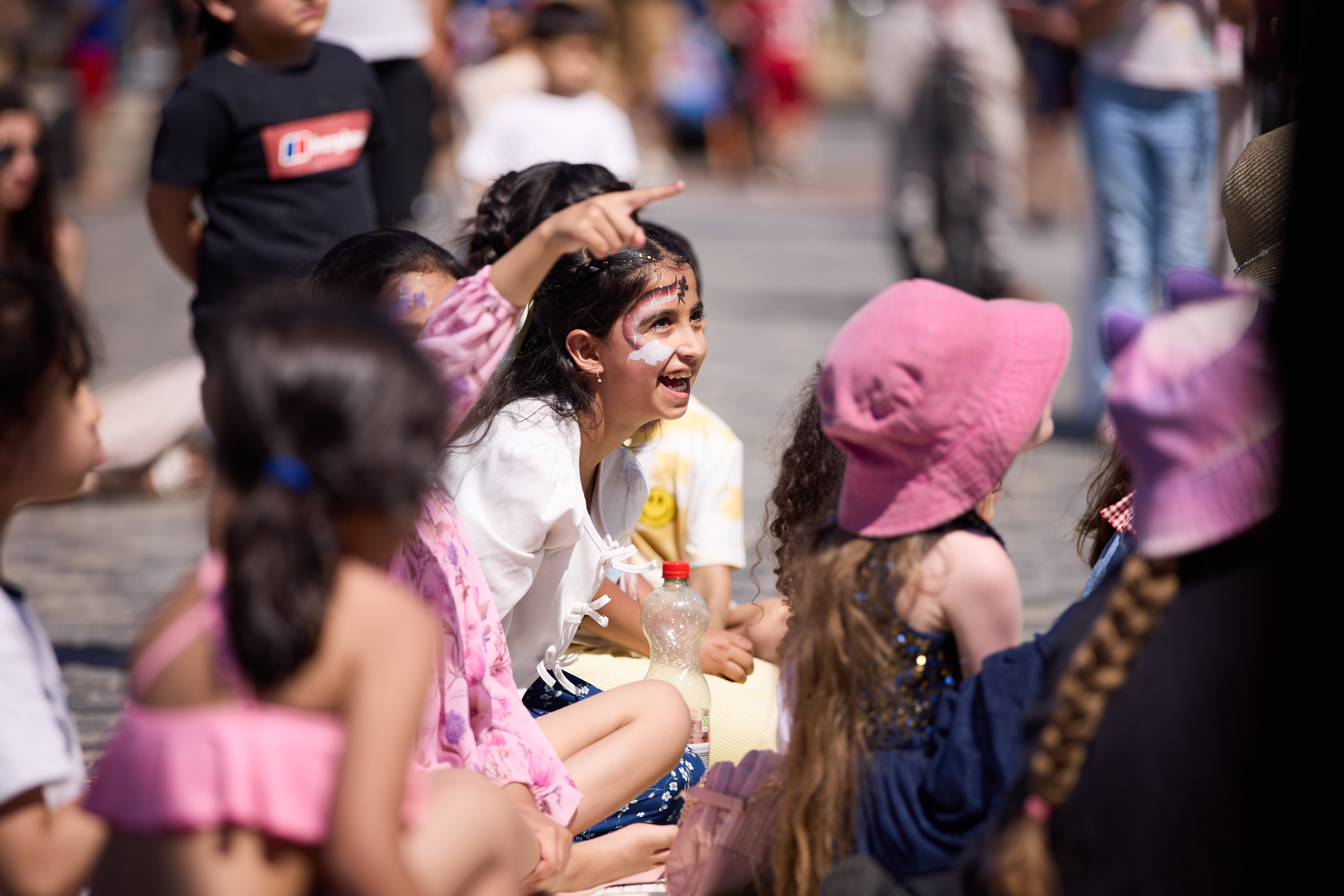 Children sitting on cobblestone street enjoying a sunny festival
