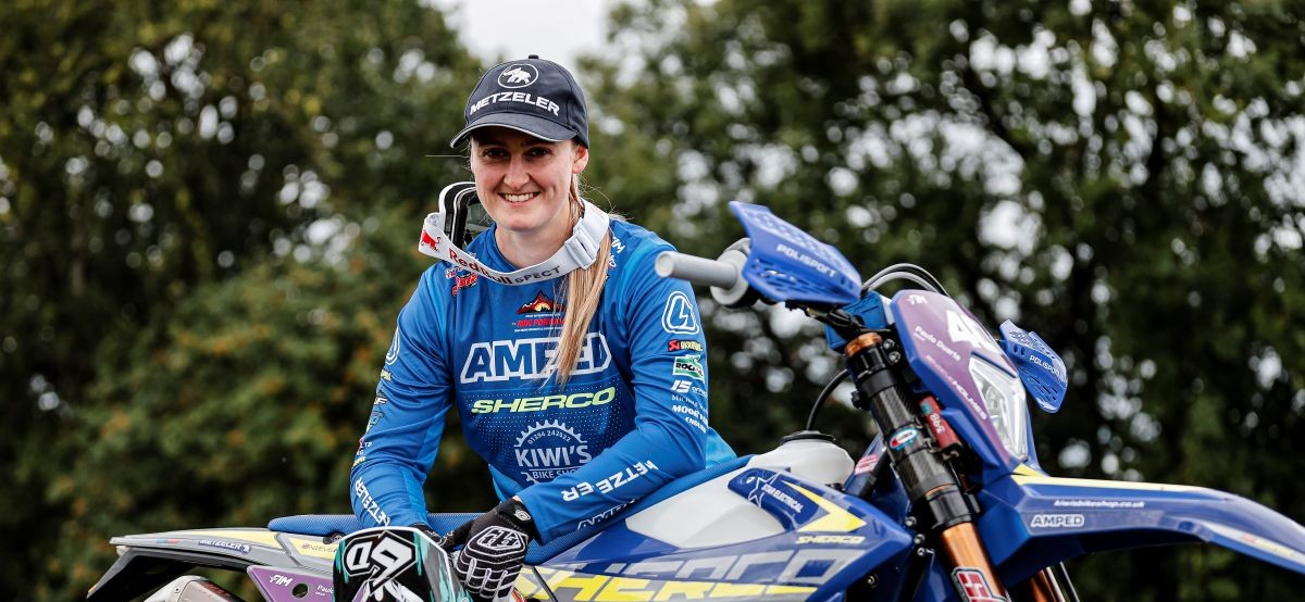 Smiling motorcyclist in blue gear with bike in lush park