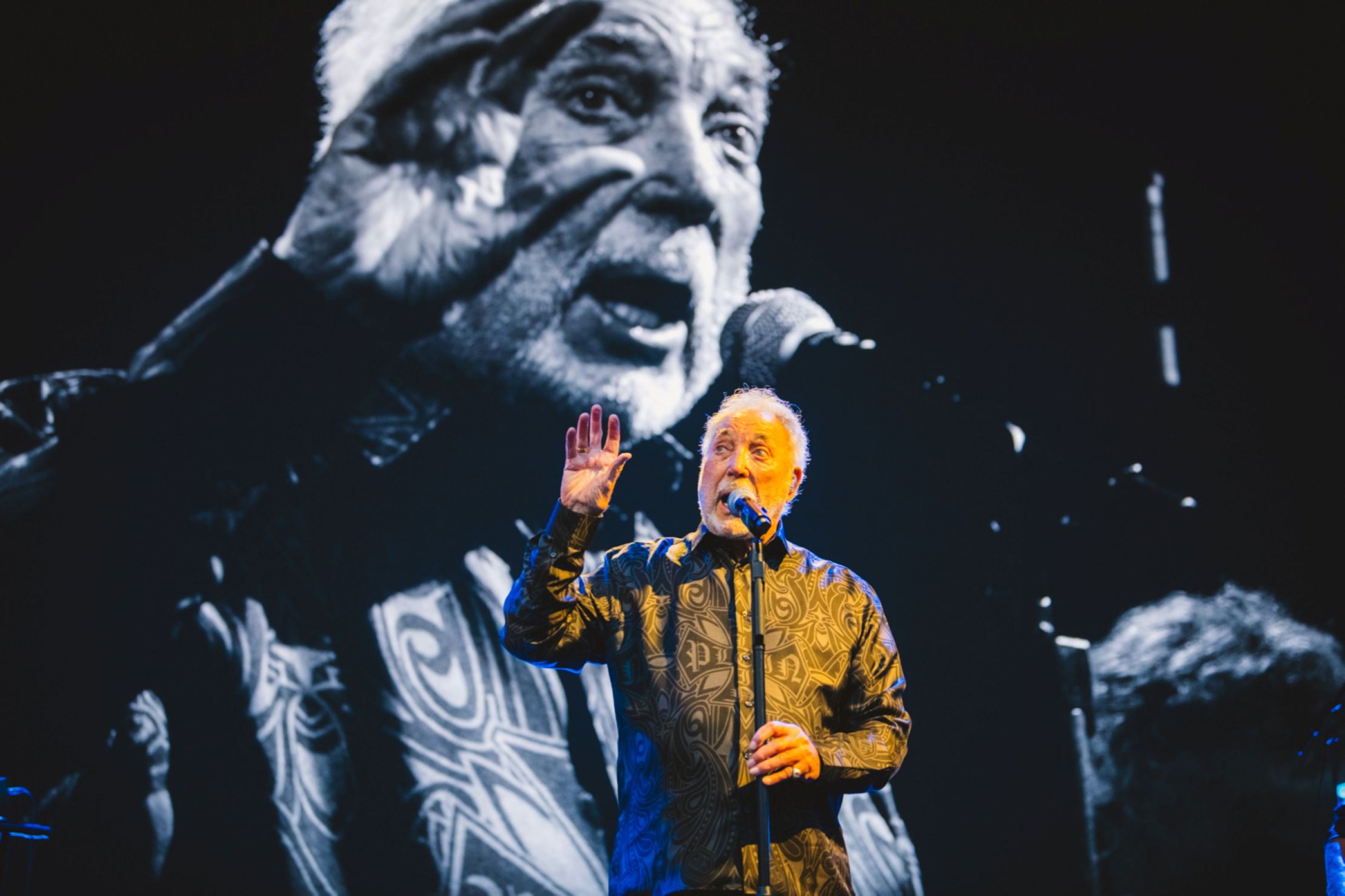 Singer performing on stage with large black and white backdrop
