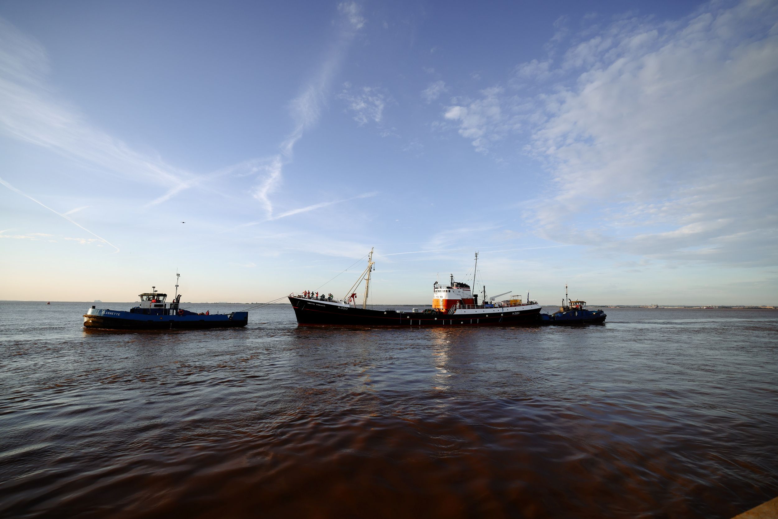 Historic trawler with two tugboats on Humber Estuary under blue sky
