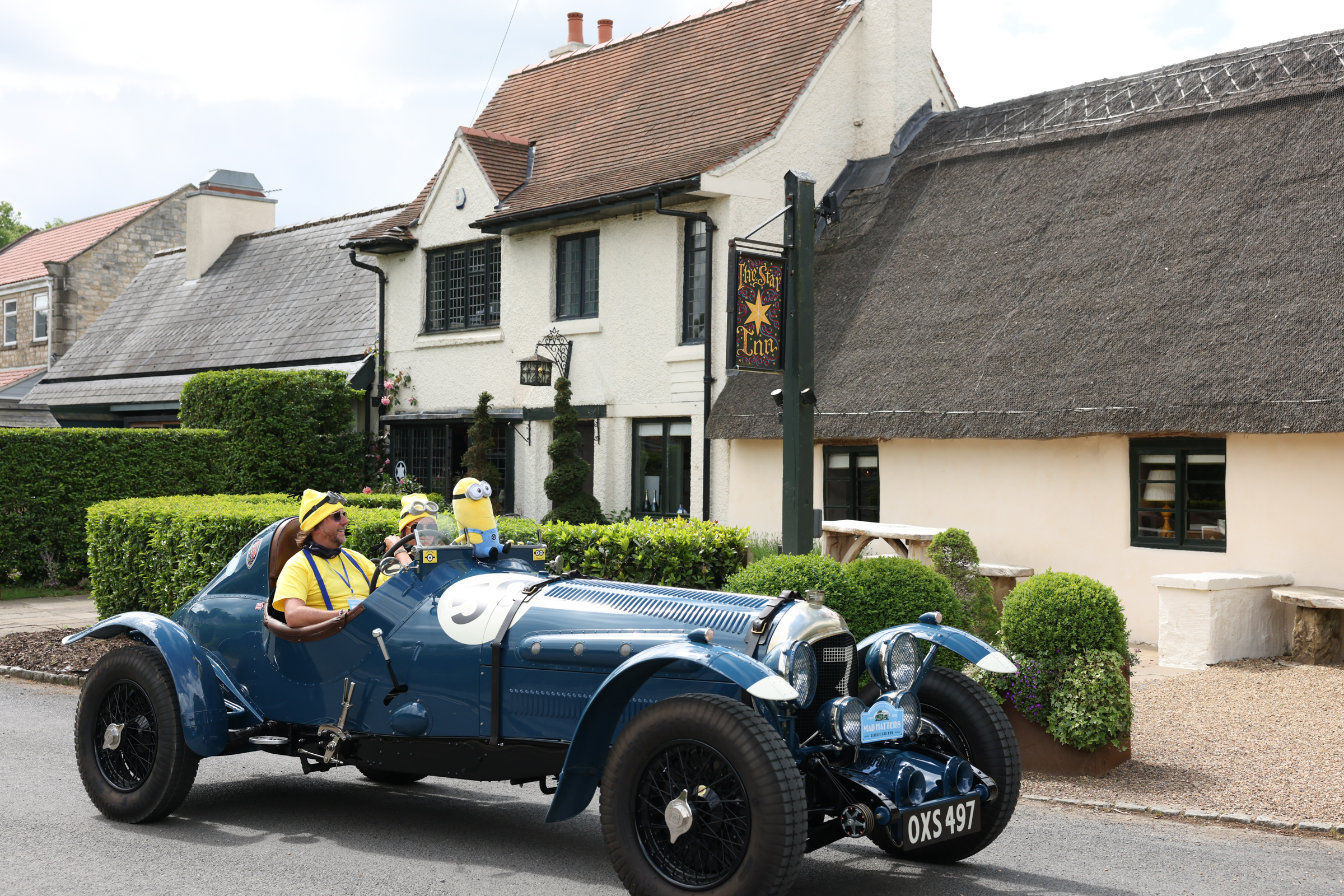 Vintage blue car with costumed drivers outside a thatched pub