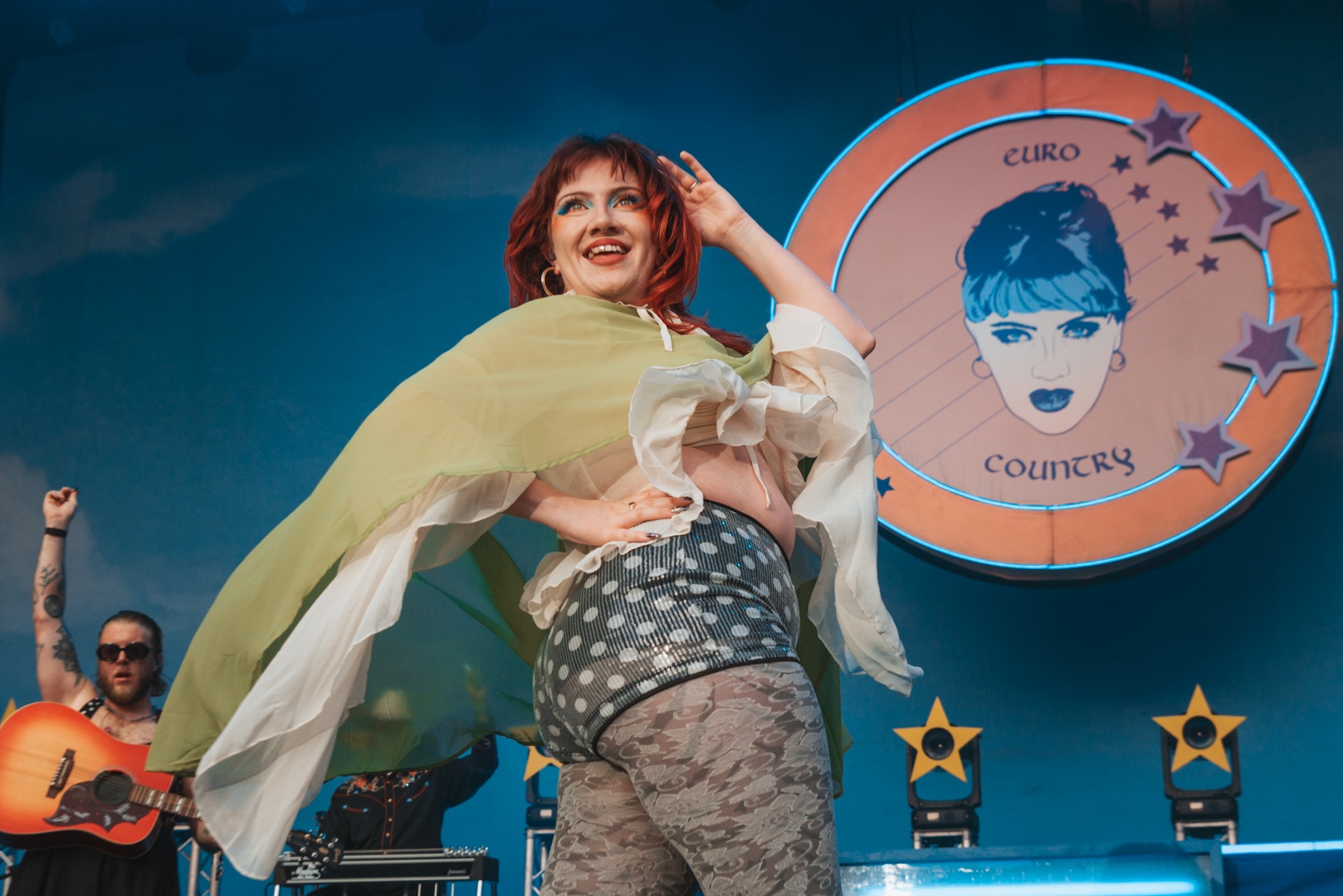 Performer in vibrant outfit on stage with colourful backdrop