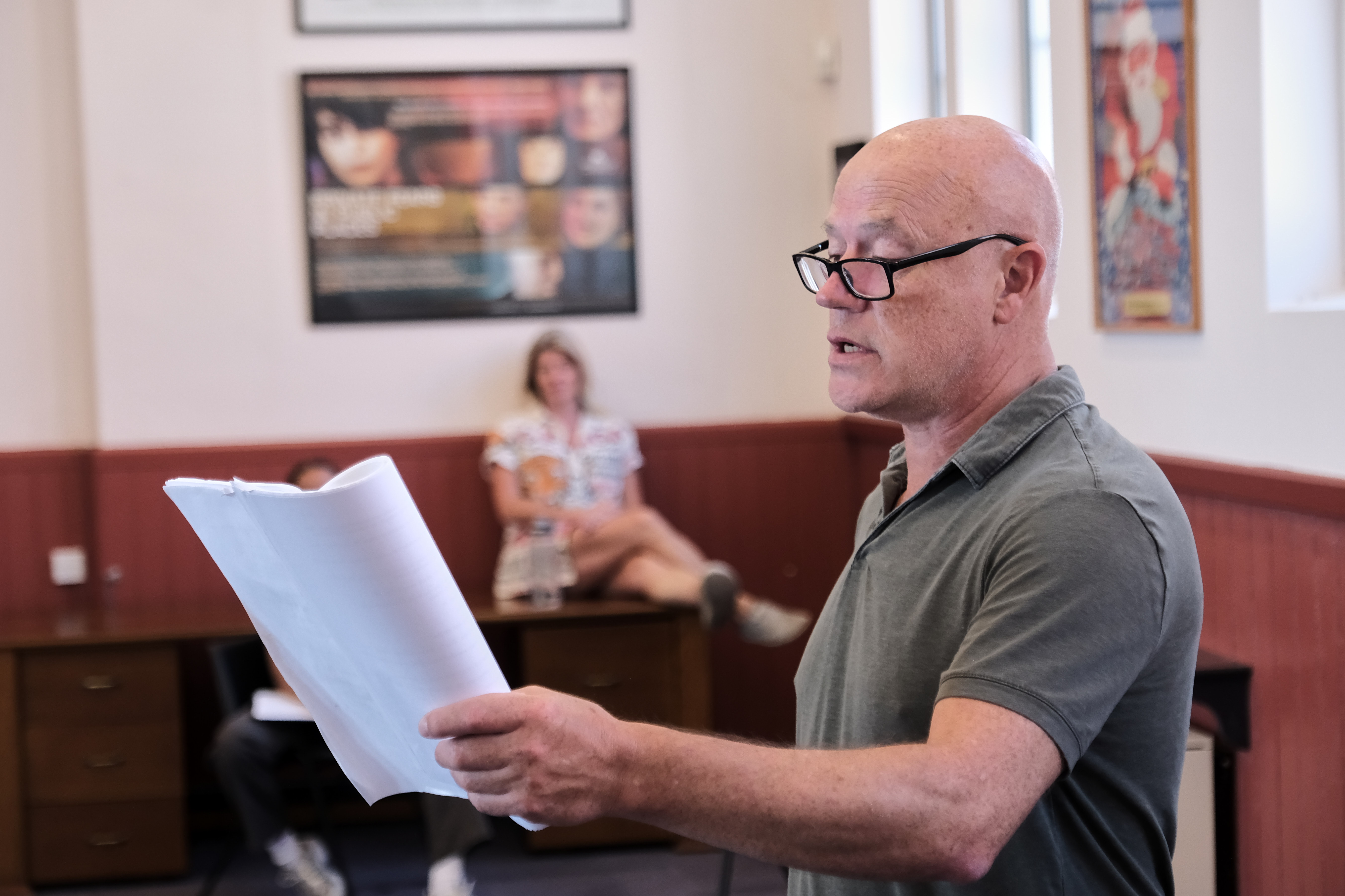 Bald man with glasses reading a script in a rehearsal room