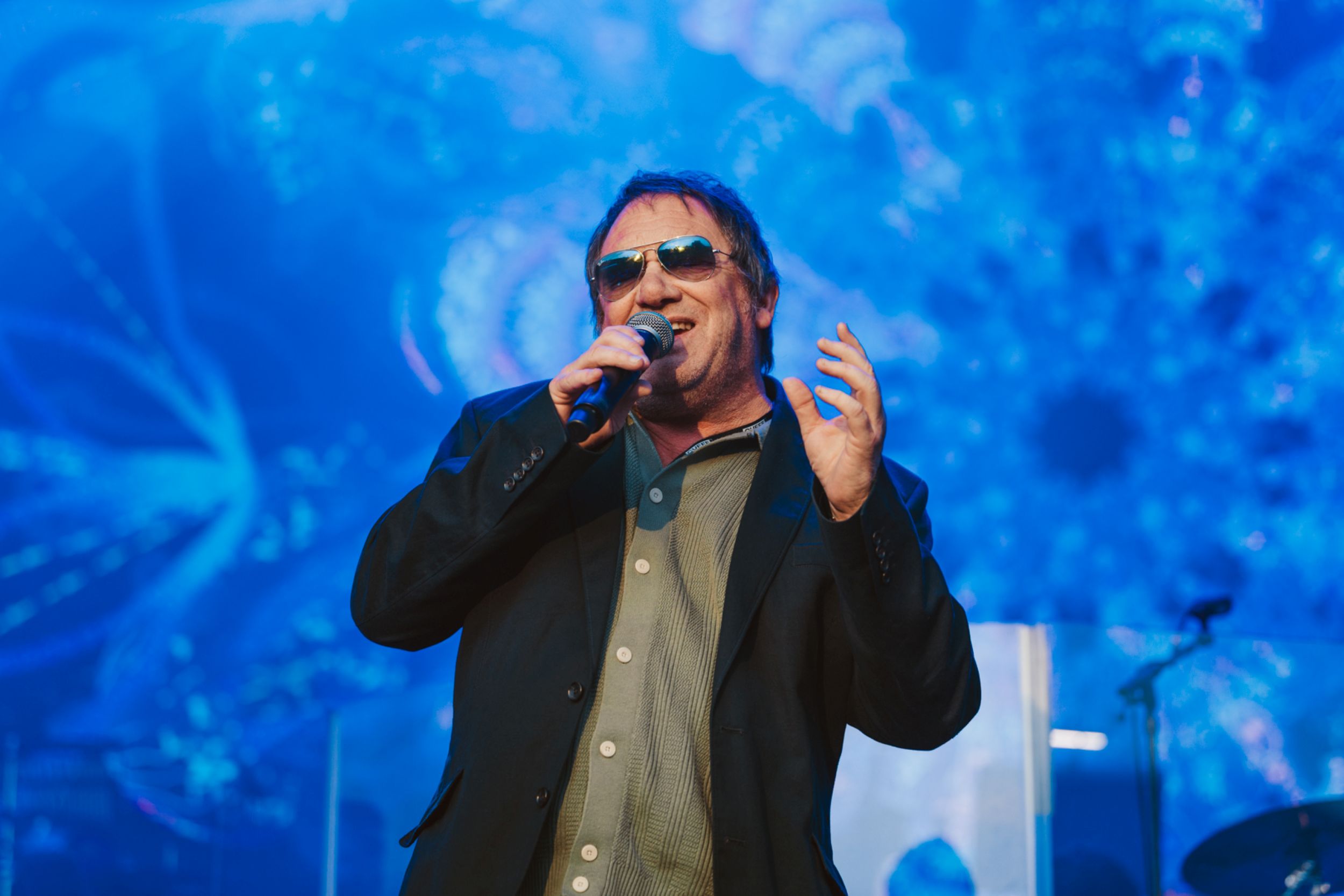 Man in sunglasses singing on stage with blue patterned backdrop