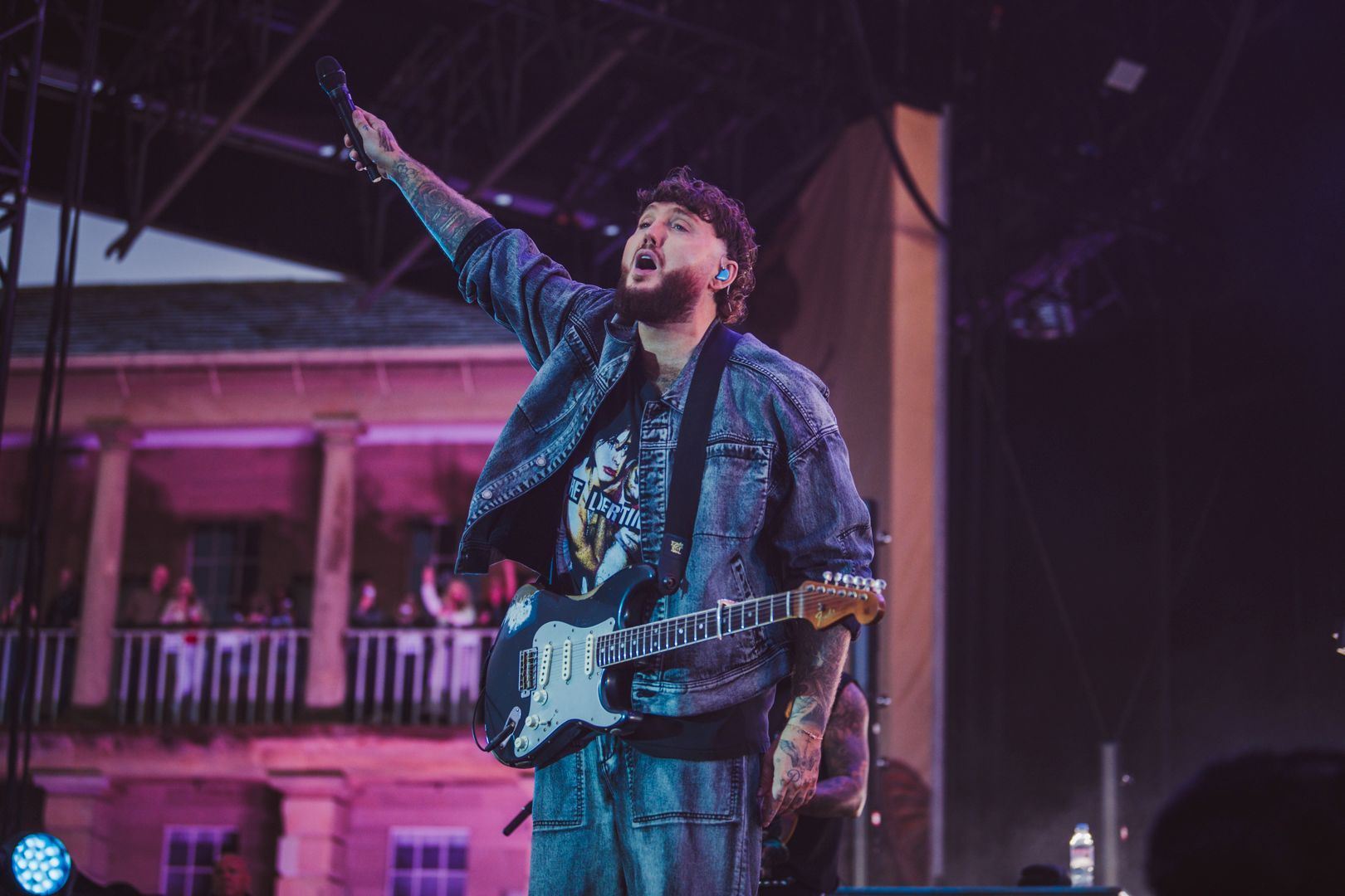 Musician in denim jacket performing on outdoor stage