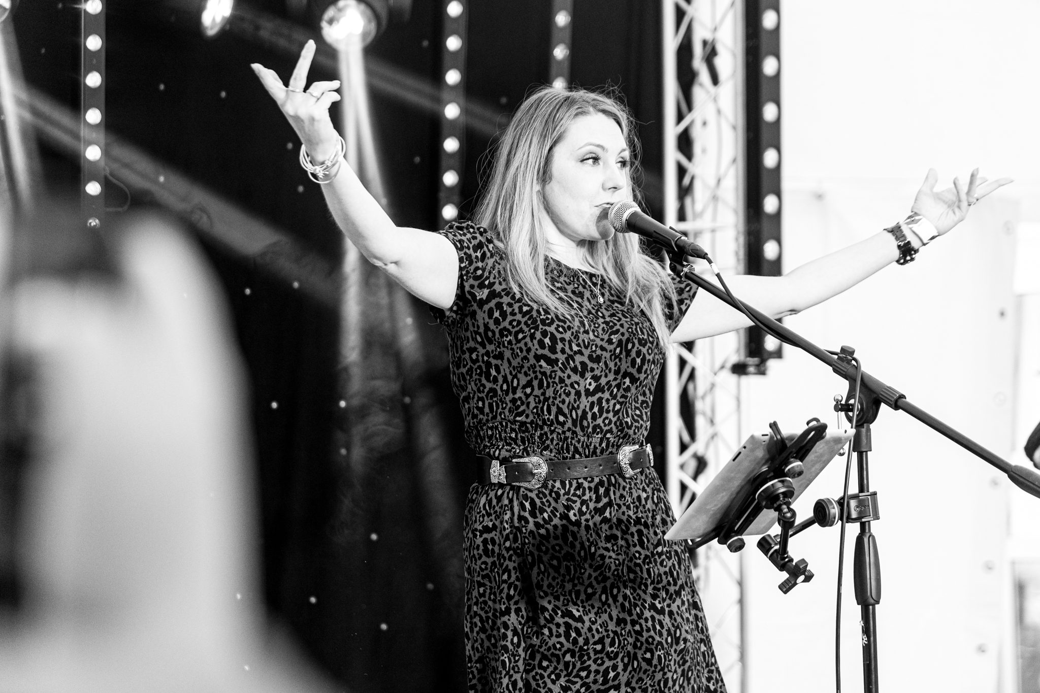 Woman singing on stage with arms raised, microphone stand nearby