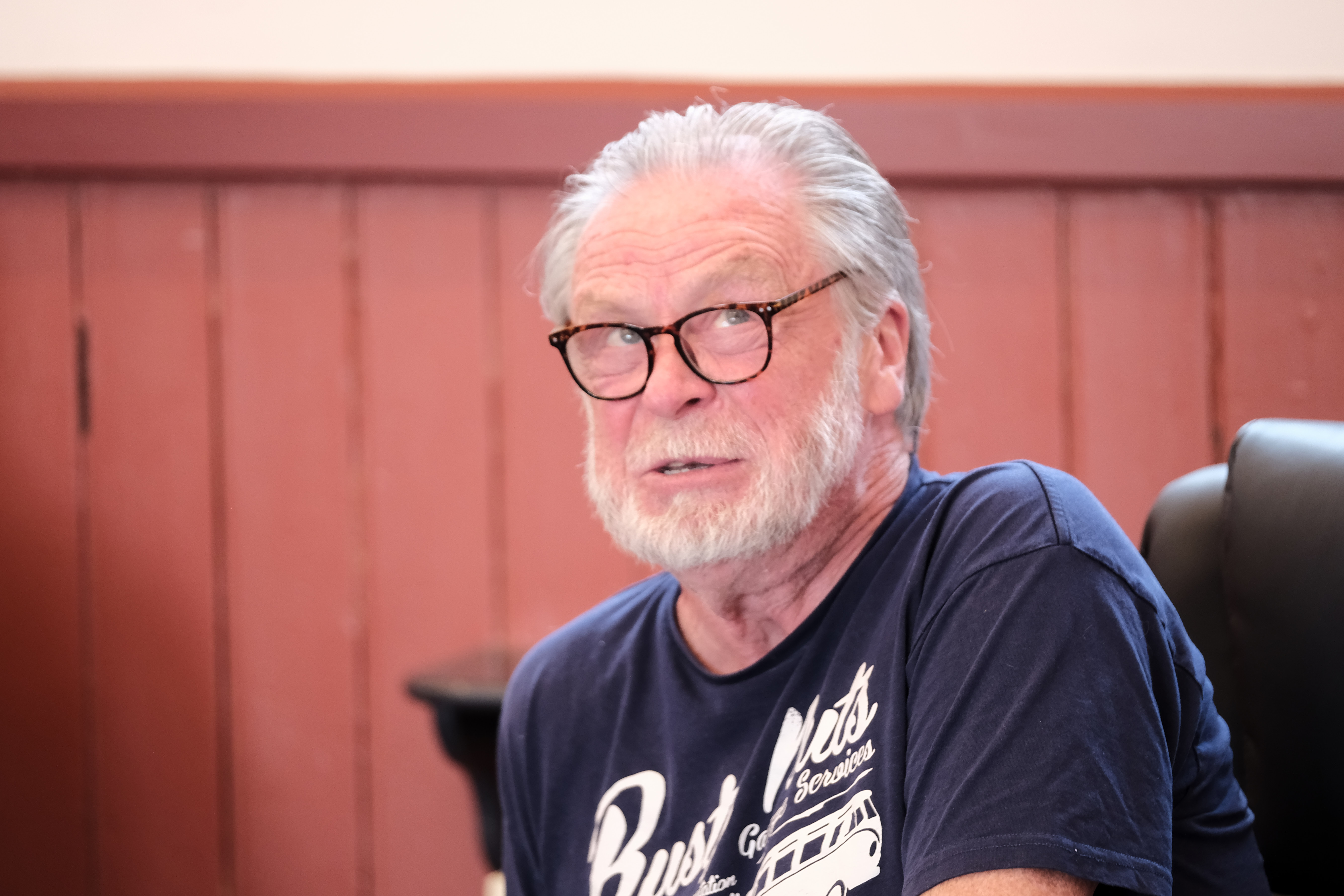 Elderly man with glasses and beard wearing a navy t-shirt