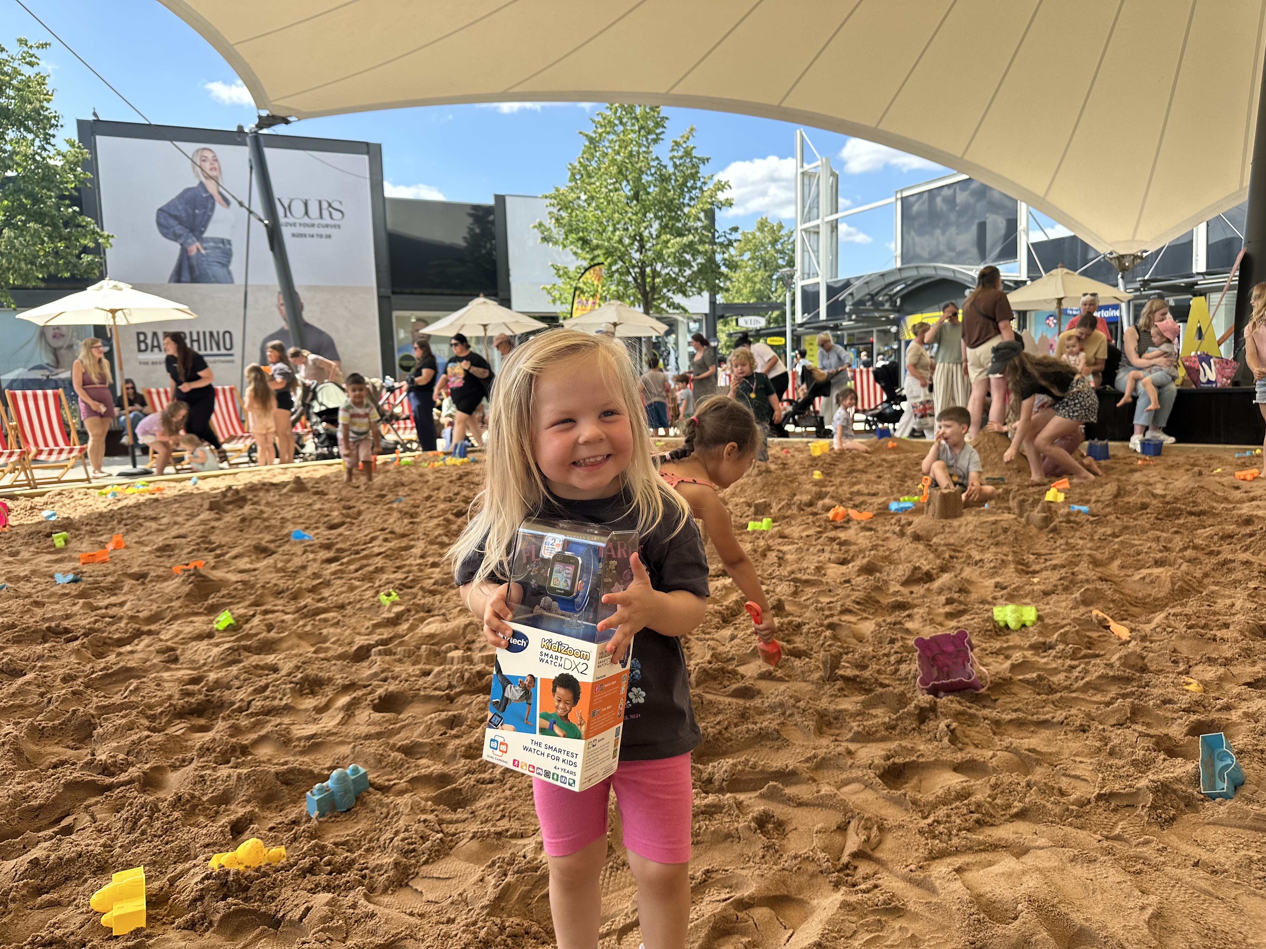 Smiling child holding toy in outdoor urban sand play area