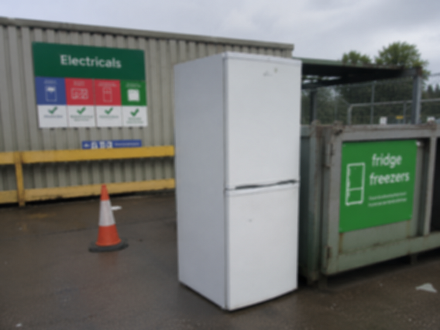 Outdoor recycling centre with a white fridge near containers