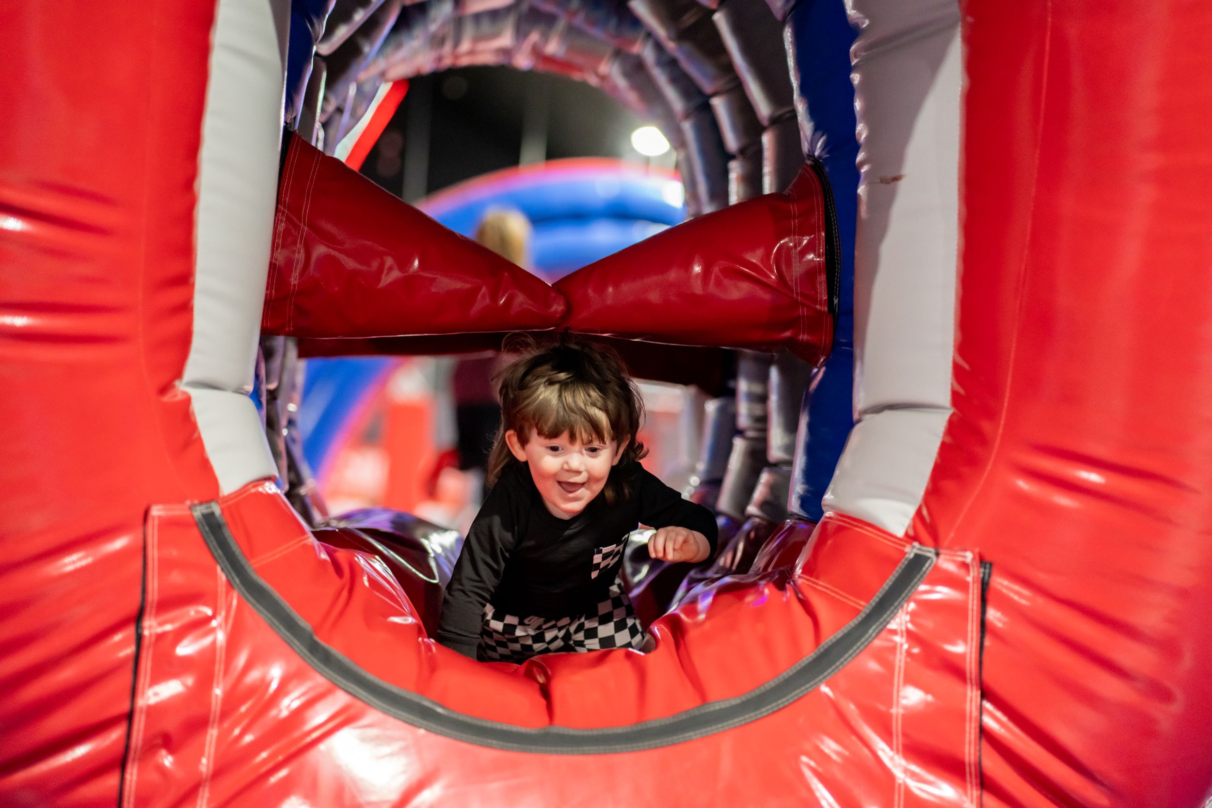 Child crawling through inflatable red tunnel at play center