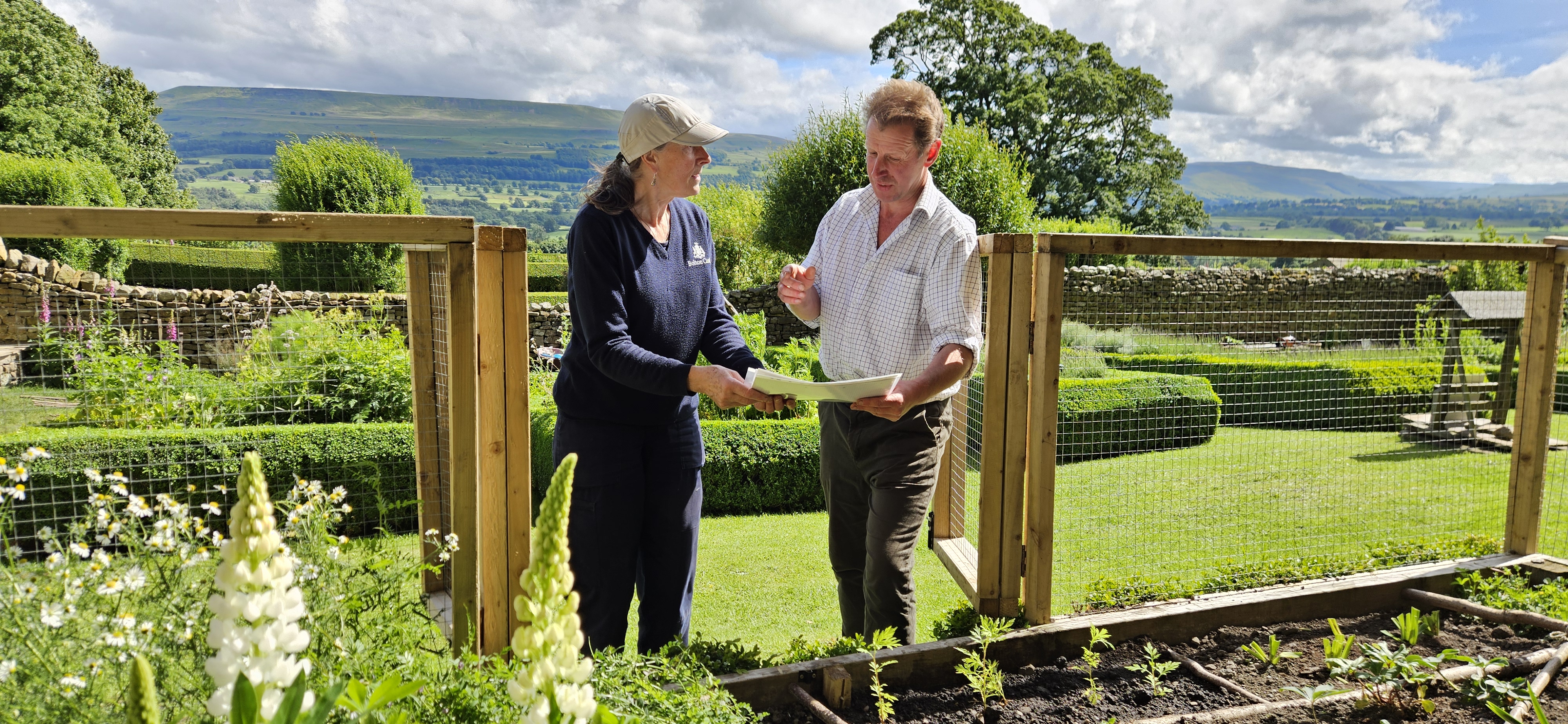 Two people discussing garden plans in a lush countryside setting