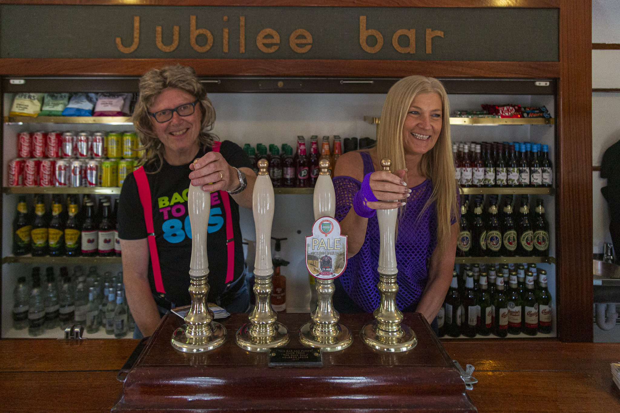 Two people smiling behind a traditional English pub bar