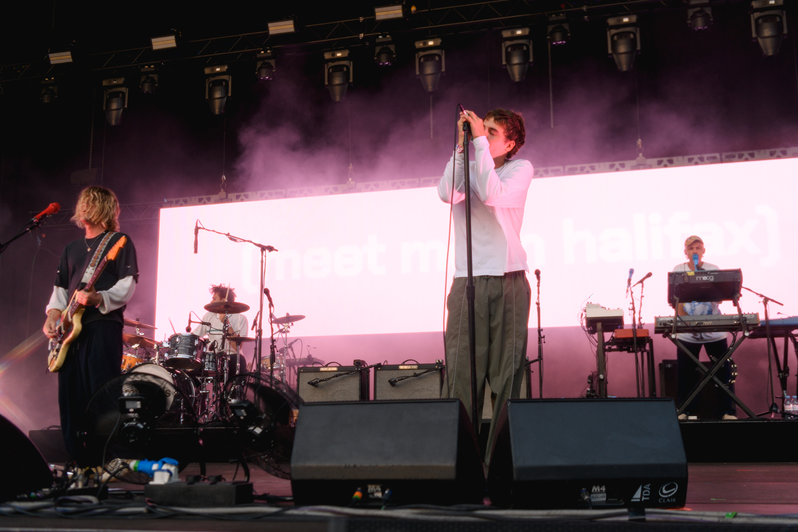 Live band performing on stage with pink lighting and instruments