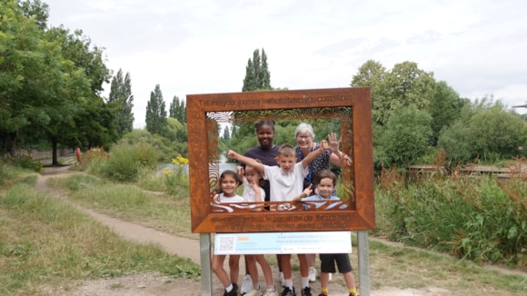 Family posing in wooden frame at park with trees and path